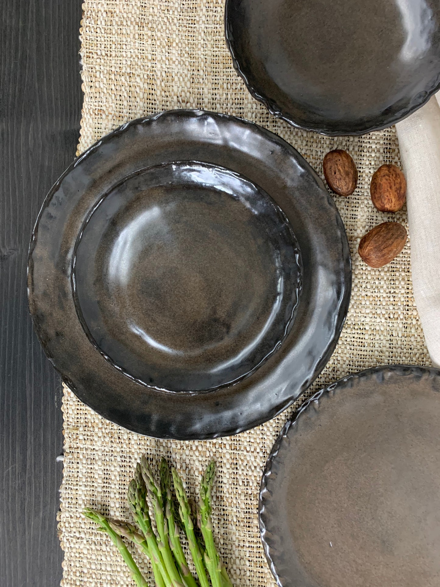Set of black ceramic plates on a textured surface with asparagus and almonds.