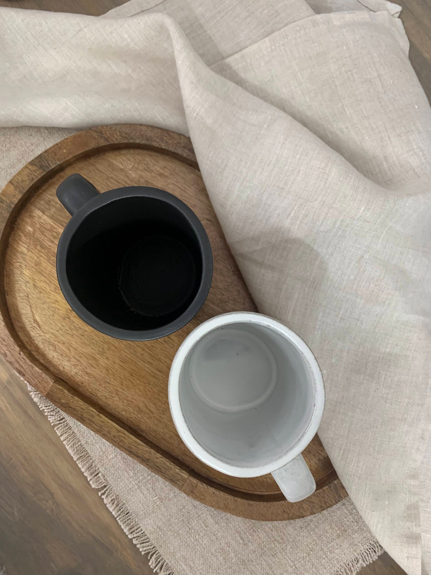 Two artisan handcrafted pottery mugs on a wooden tray with a beige cloth background