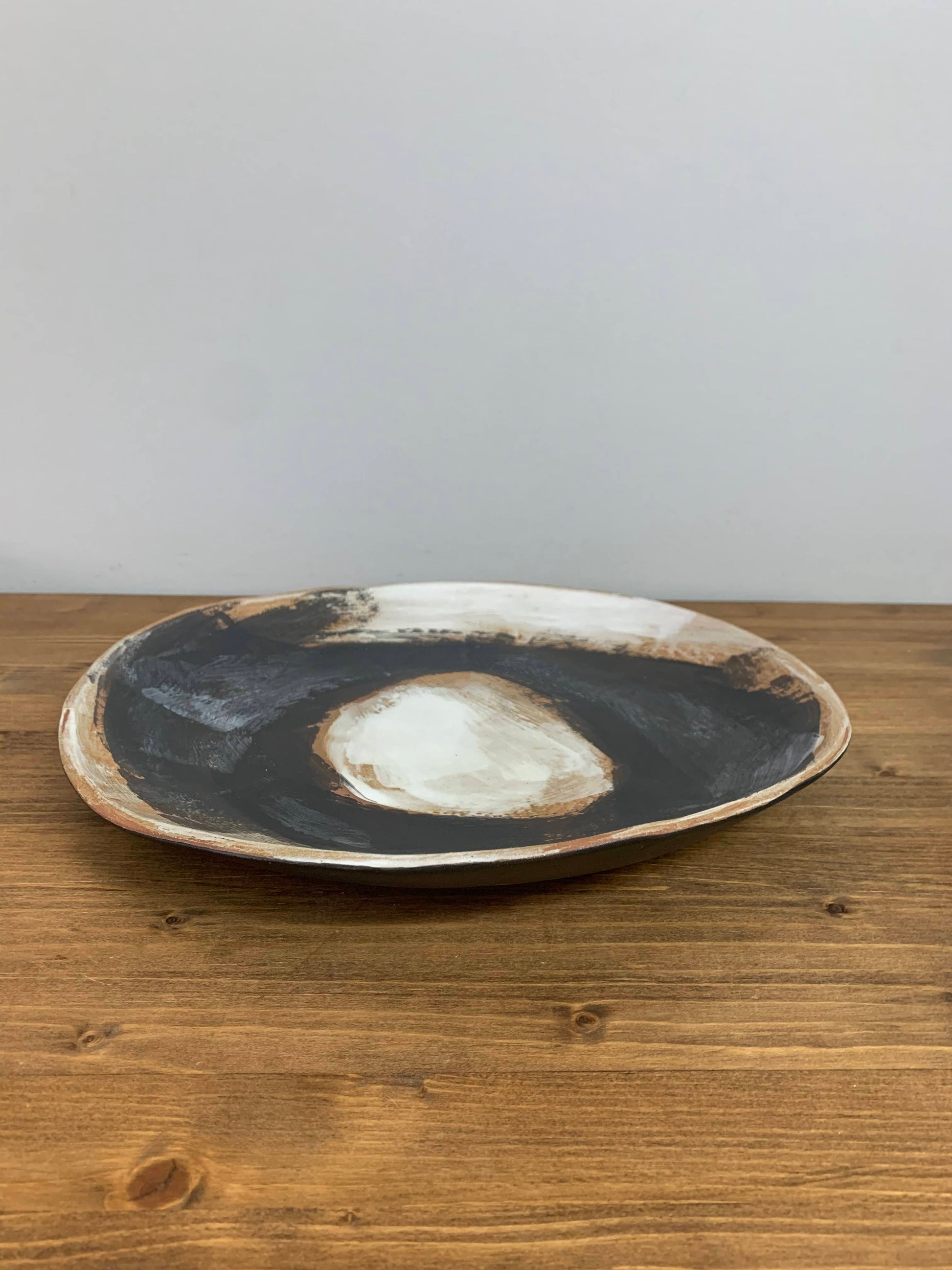 Ceramic art shallow bowl with black, brown and white circular design on a wood surface and light gray background