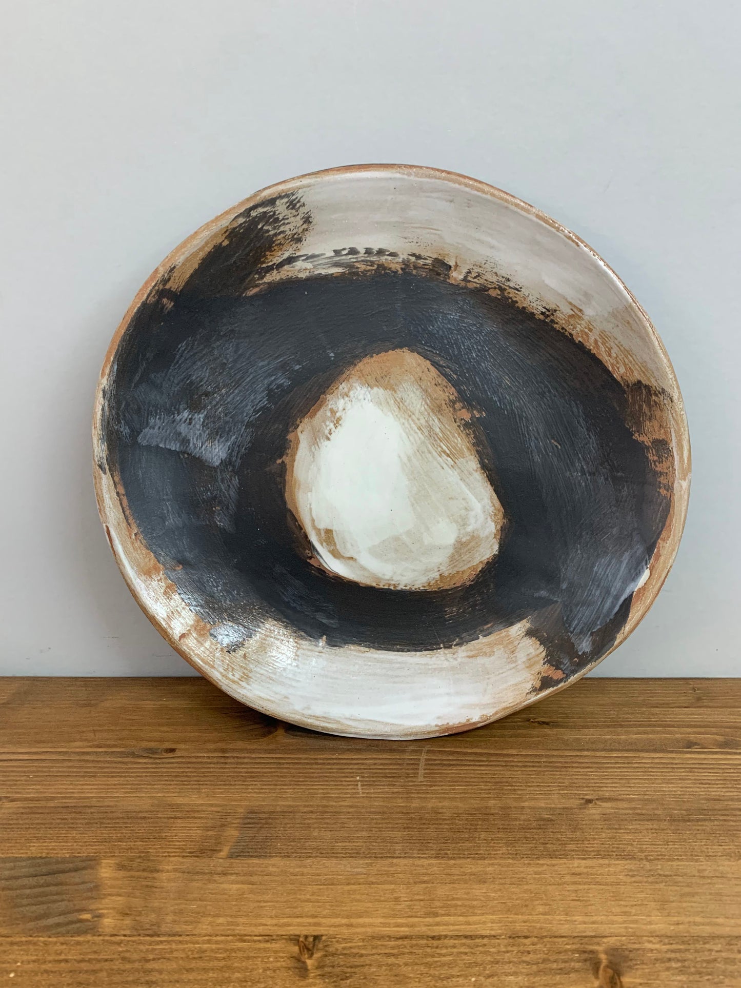 Ceramic art bowl with black, brown and white circular design on a light gray background