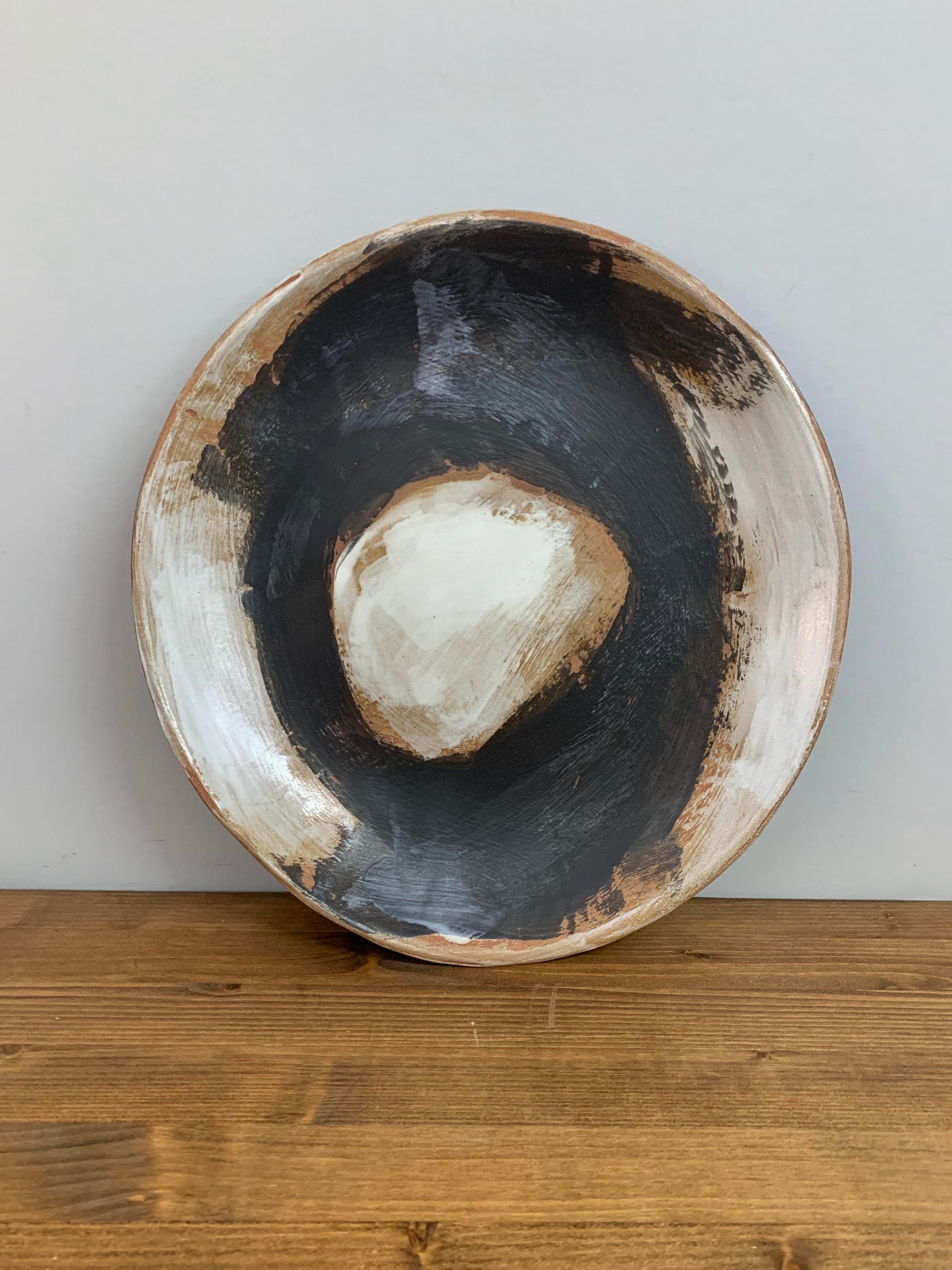 Ceramic art bowl with black, brown and white circular design on a light gray background