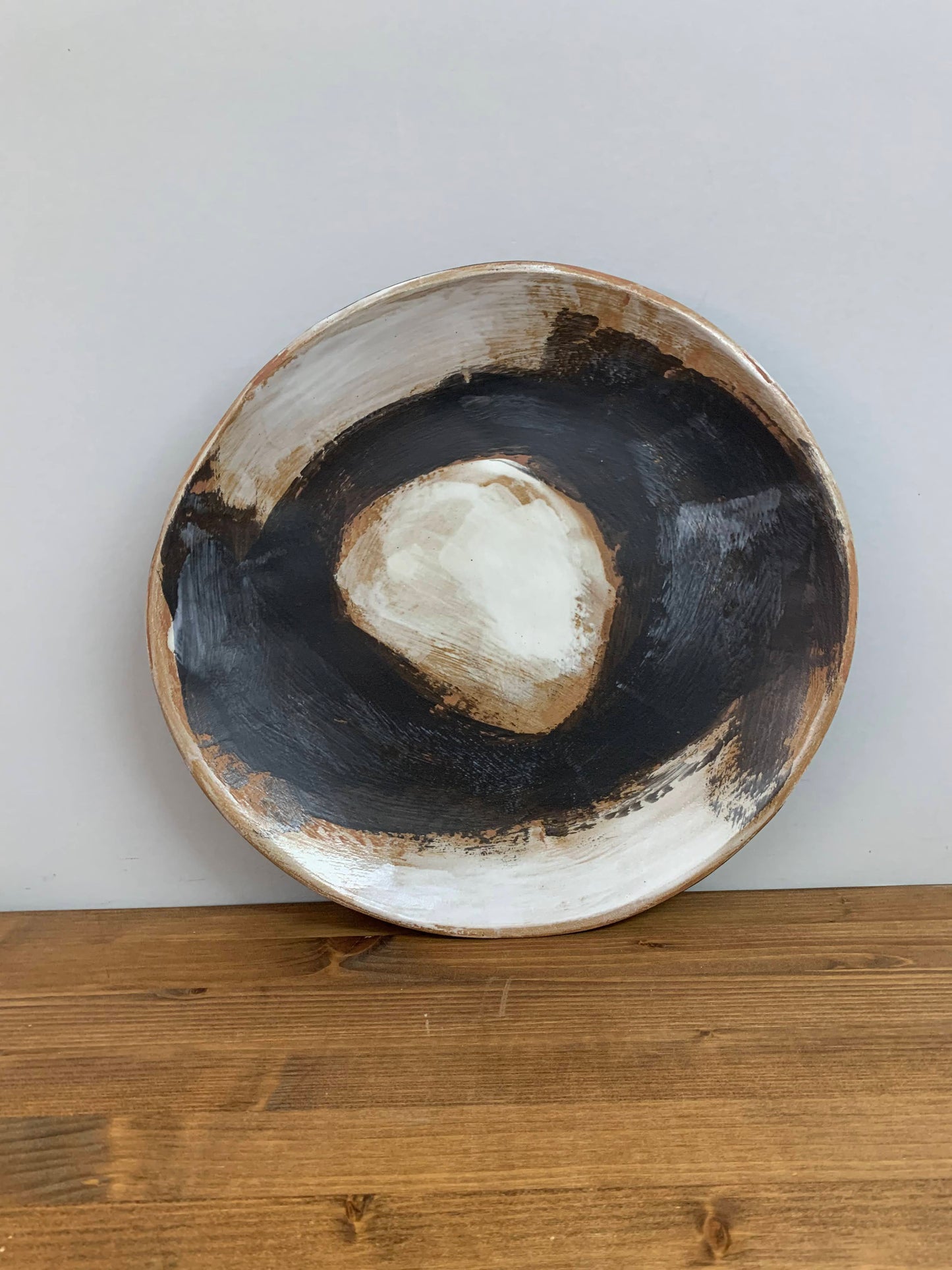 Ceramic art bowl with black, brown and white circular design on a light gray background