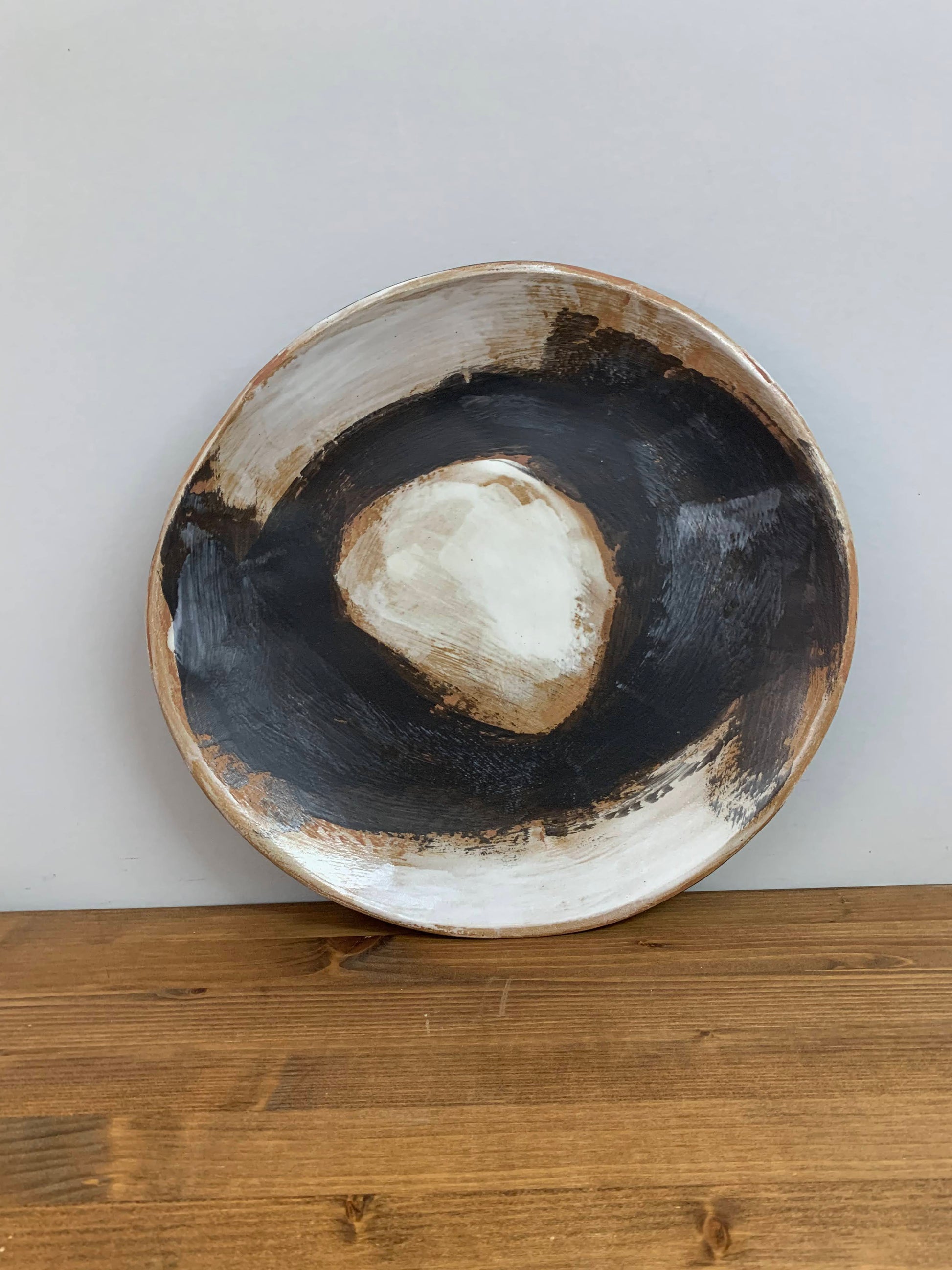 Ceramic art bowl with black, brown and white circular design on a light gray background