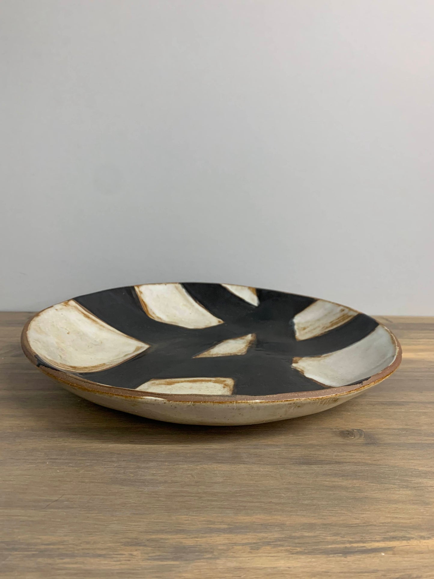 Decorative ceramic art plate with black and white abstract design on a wooden surface