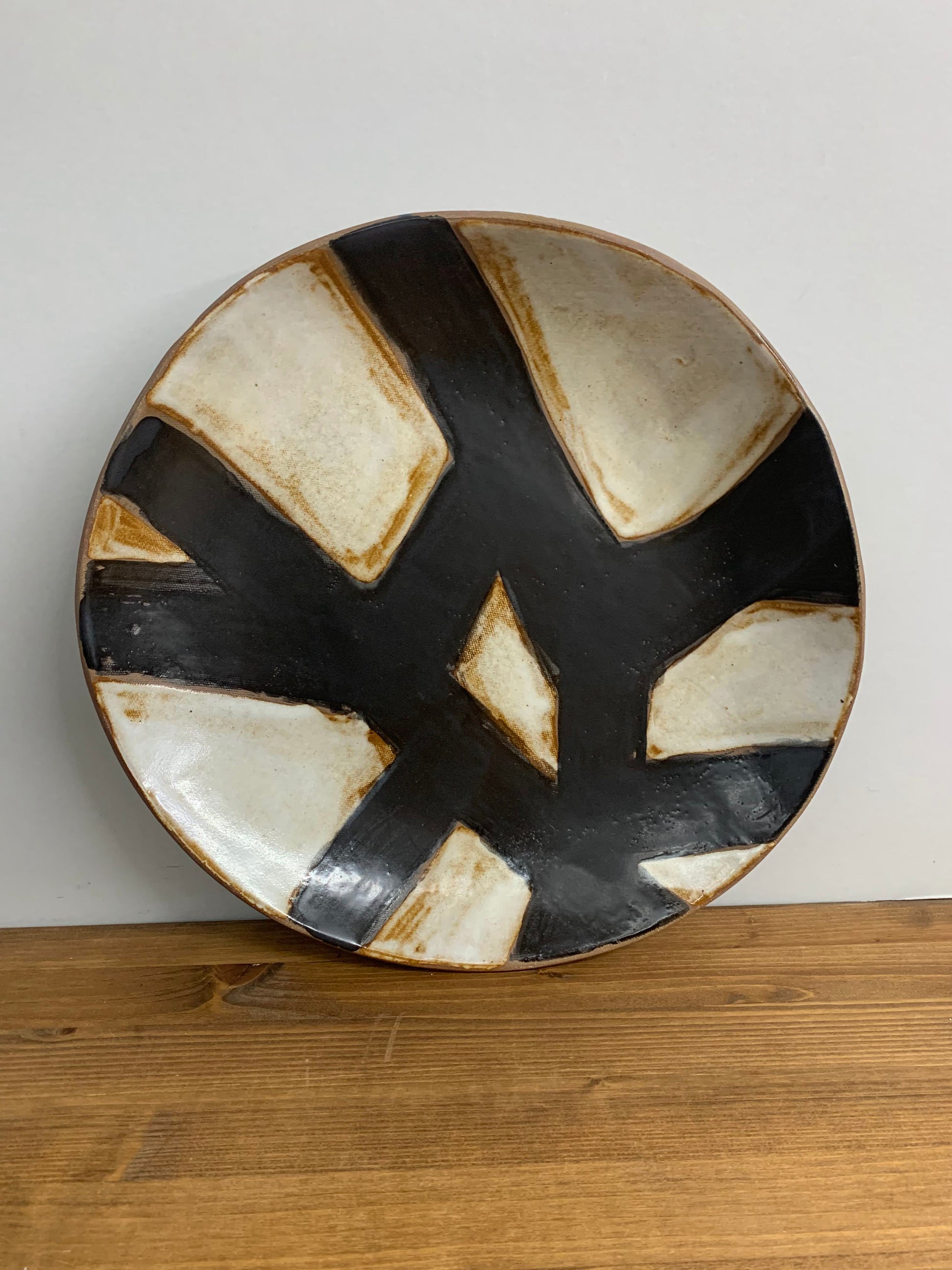 Handcrafted ceramic art plate with black and white abstract design on a light gray background