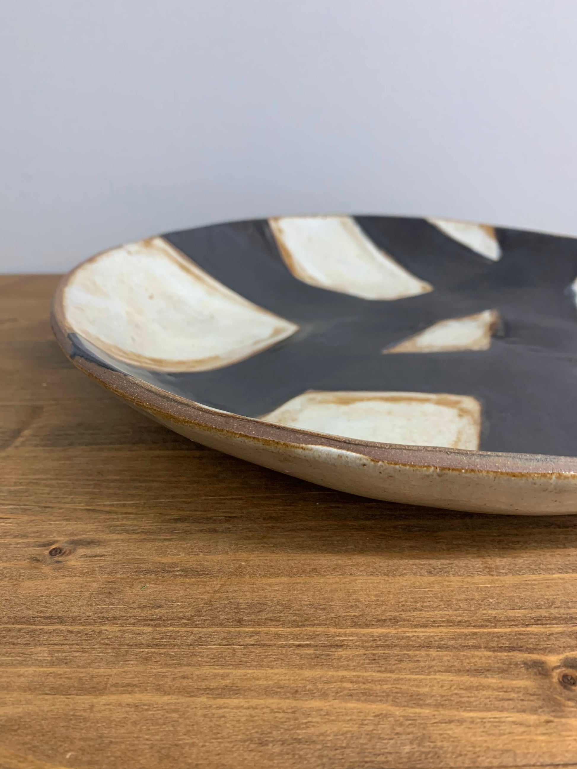 closeup of Handcrafted ceramic art plate with black and white abstract design on a light gray background
