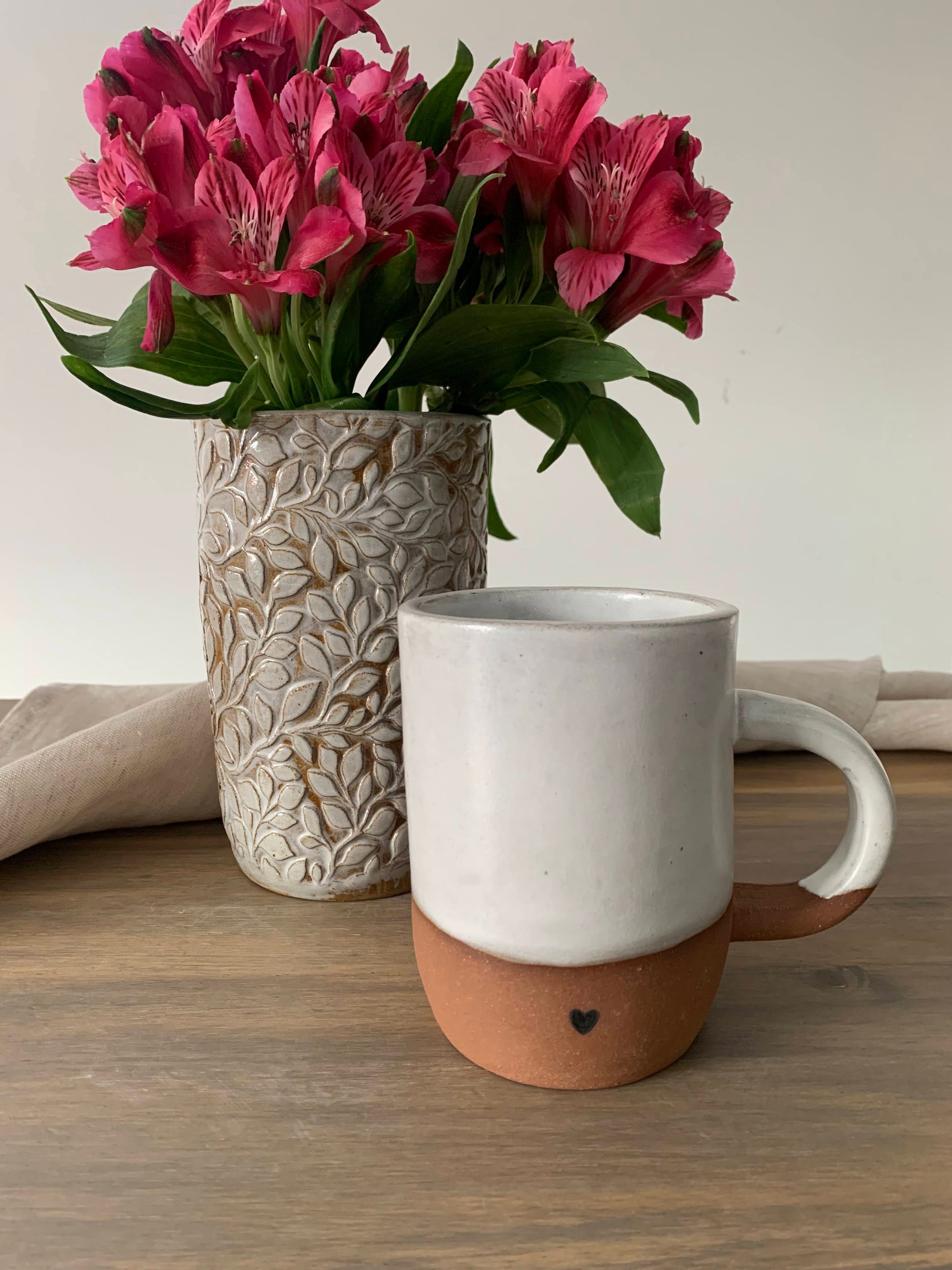 handcrafted ceramic mug next to a cylindrical vase with embossed leaf designs holding a bouquet of flowers
