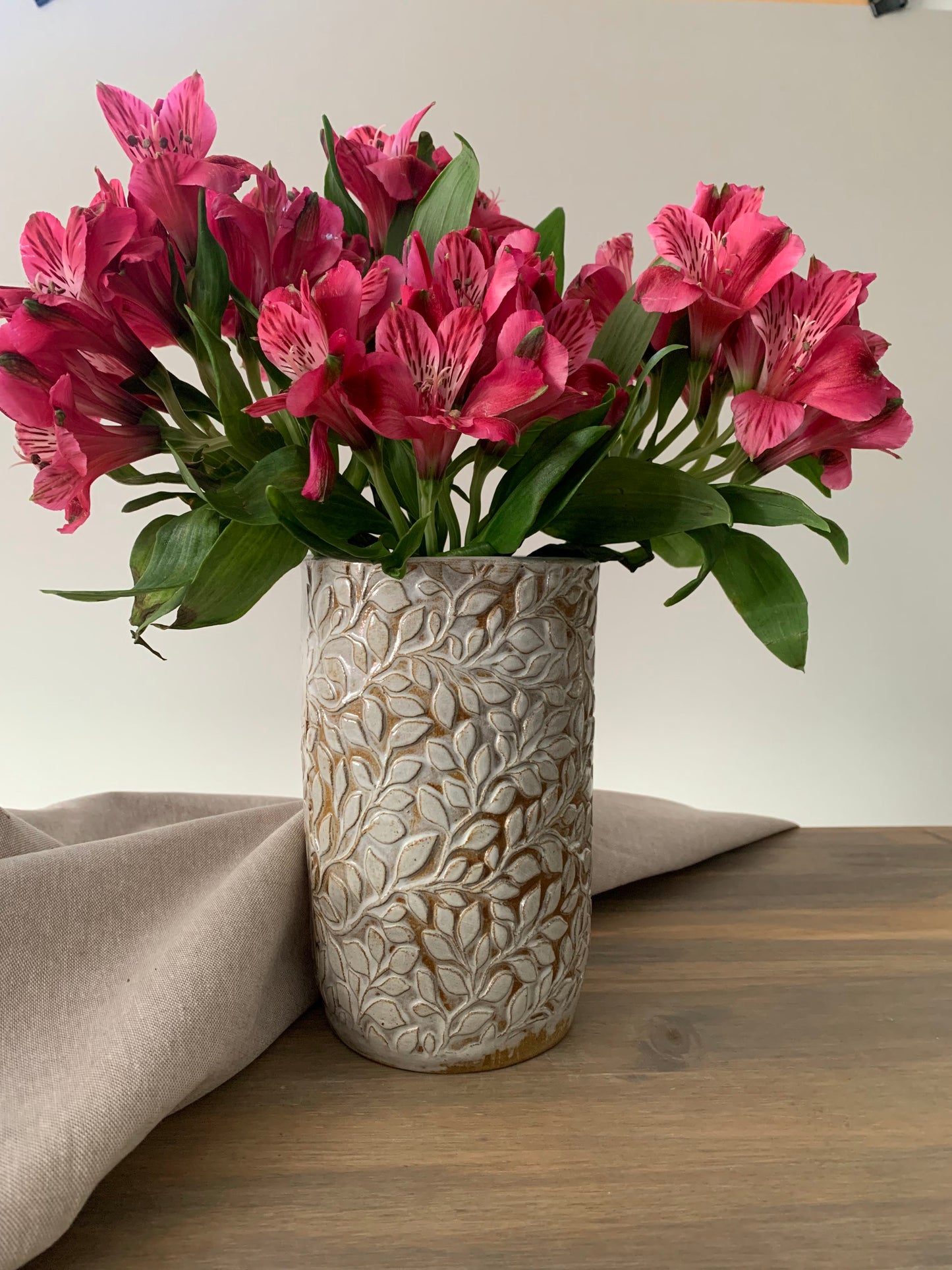 handcrafted ceramic cylindrical vase with embossed leaf designs holding a bouquet of pink flowers