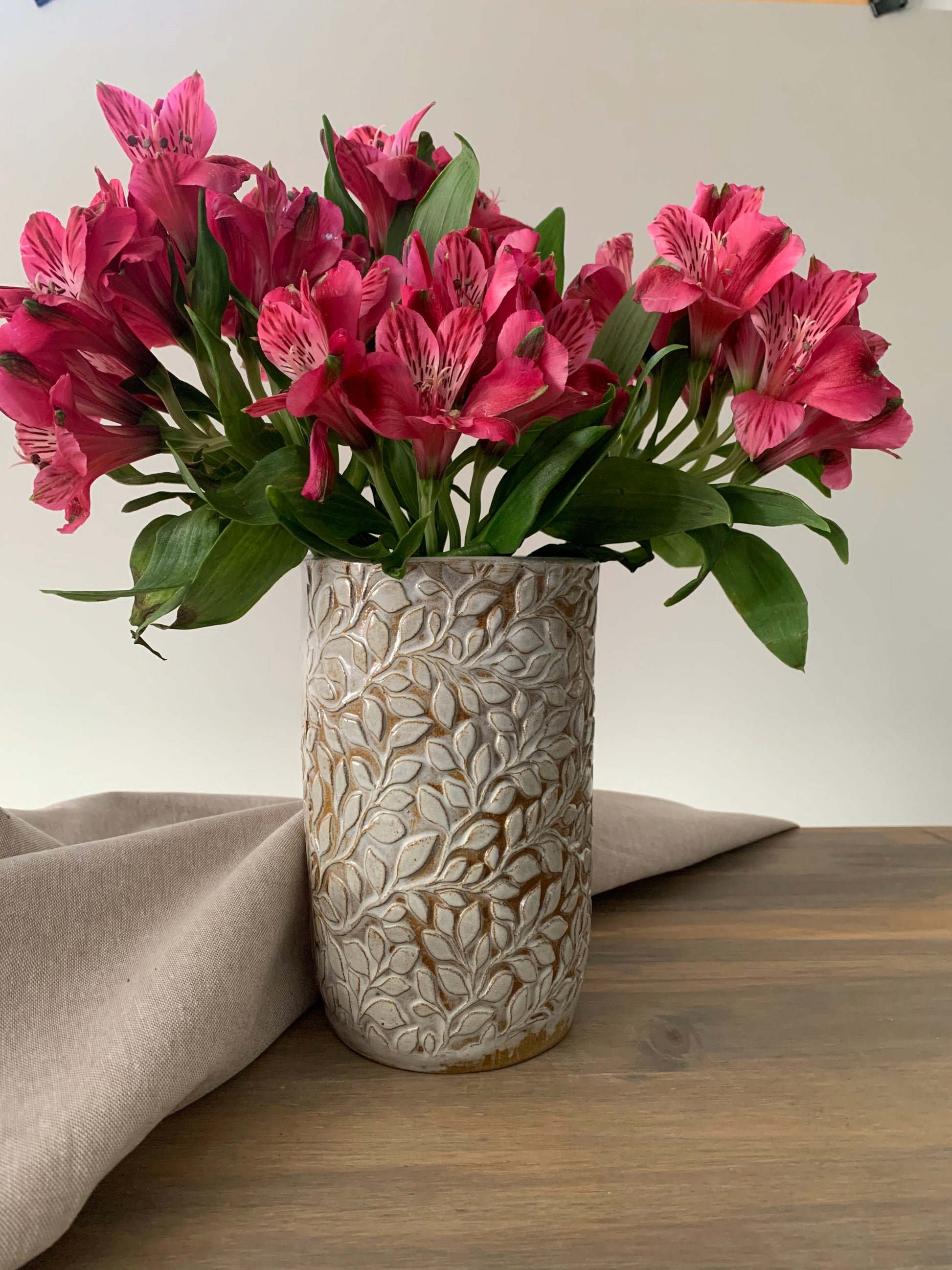 handcrafted ceramic cylindrical vase with embossed leaf designs holding a bouquet of pink flowers