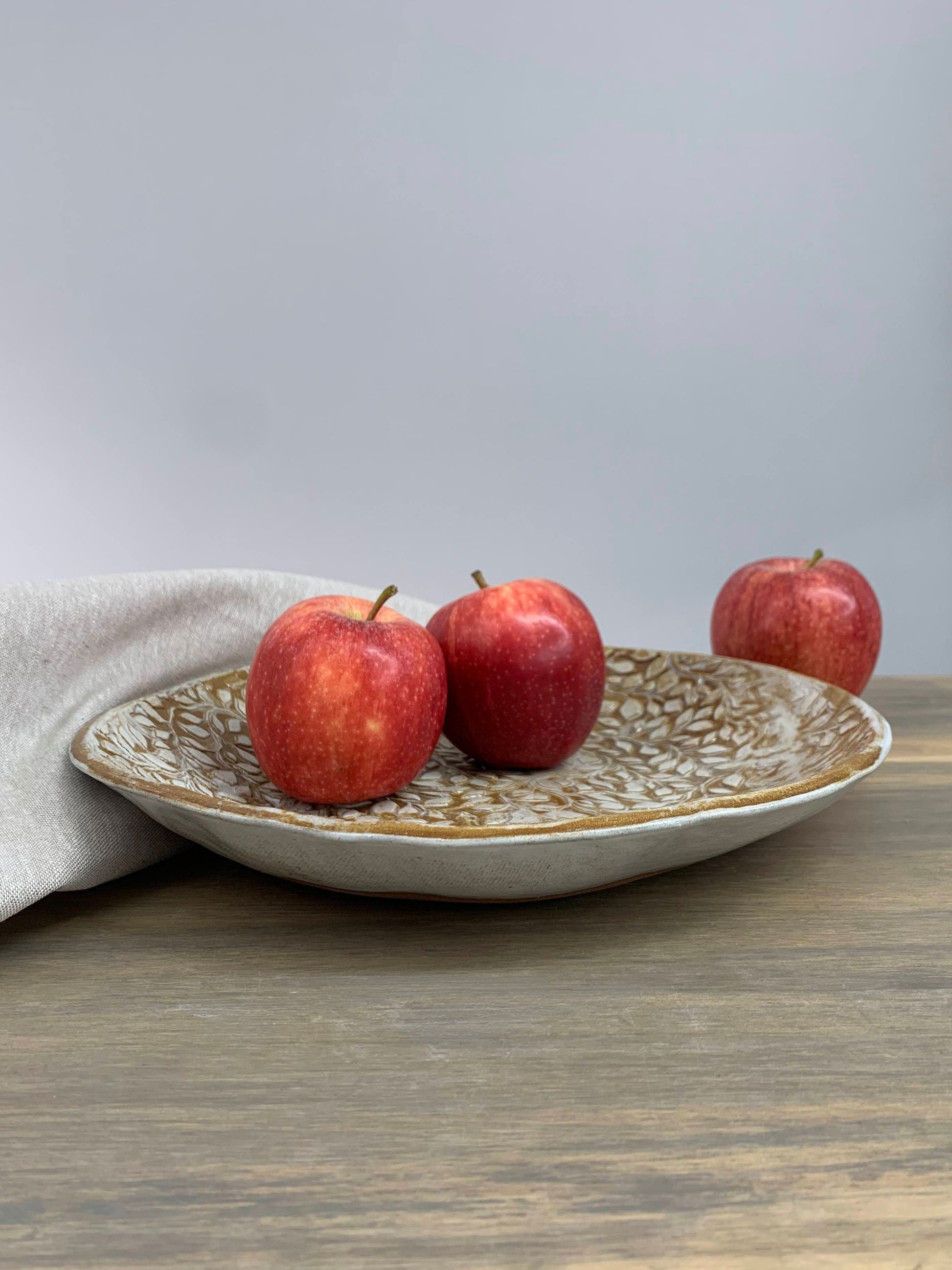 Three apples on a decorative handcrafted bowl with a gray background