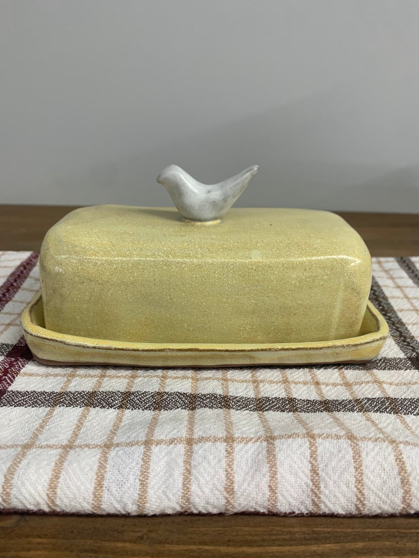 Yellow handmade ceramic butter dish with a bird on top on a checkered cloth