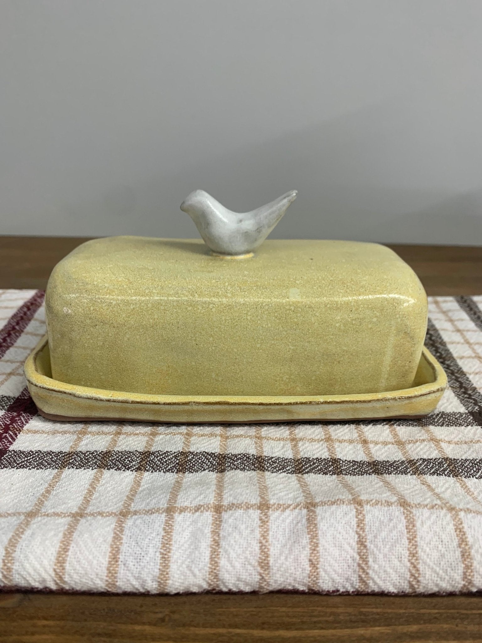 Yellow handmade ceramic butter dish with a bird on top on a checkered cloth