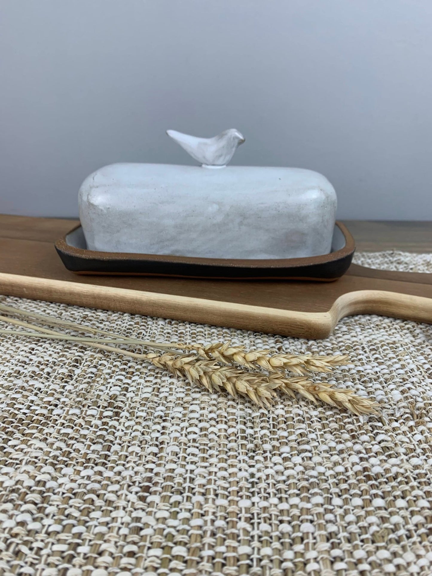 Handmade ceramic butter dish with a bird design on top, placed on a wooden surface with a neutral background.