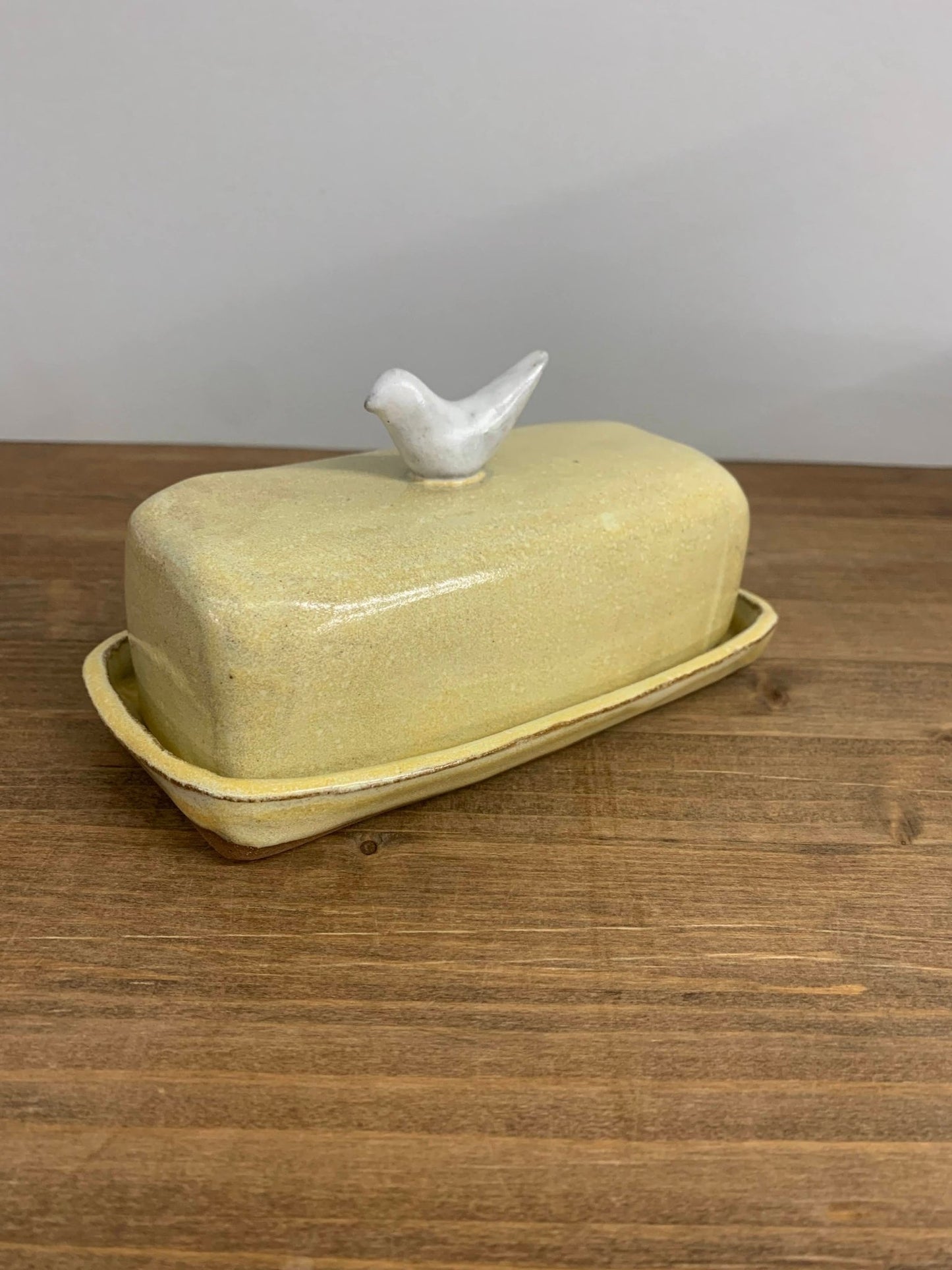 Handmade ceramic butter dish with a bird on top on a wooden surface