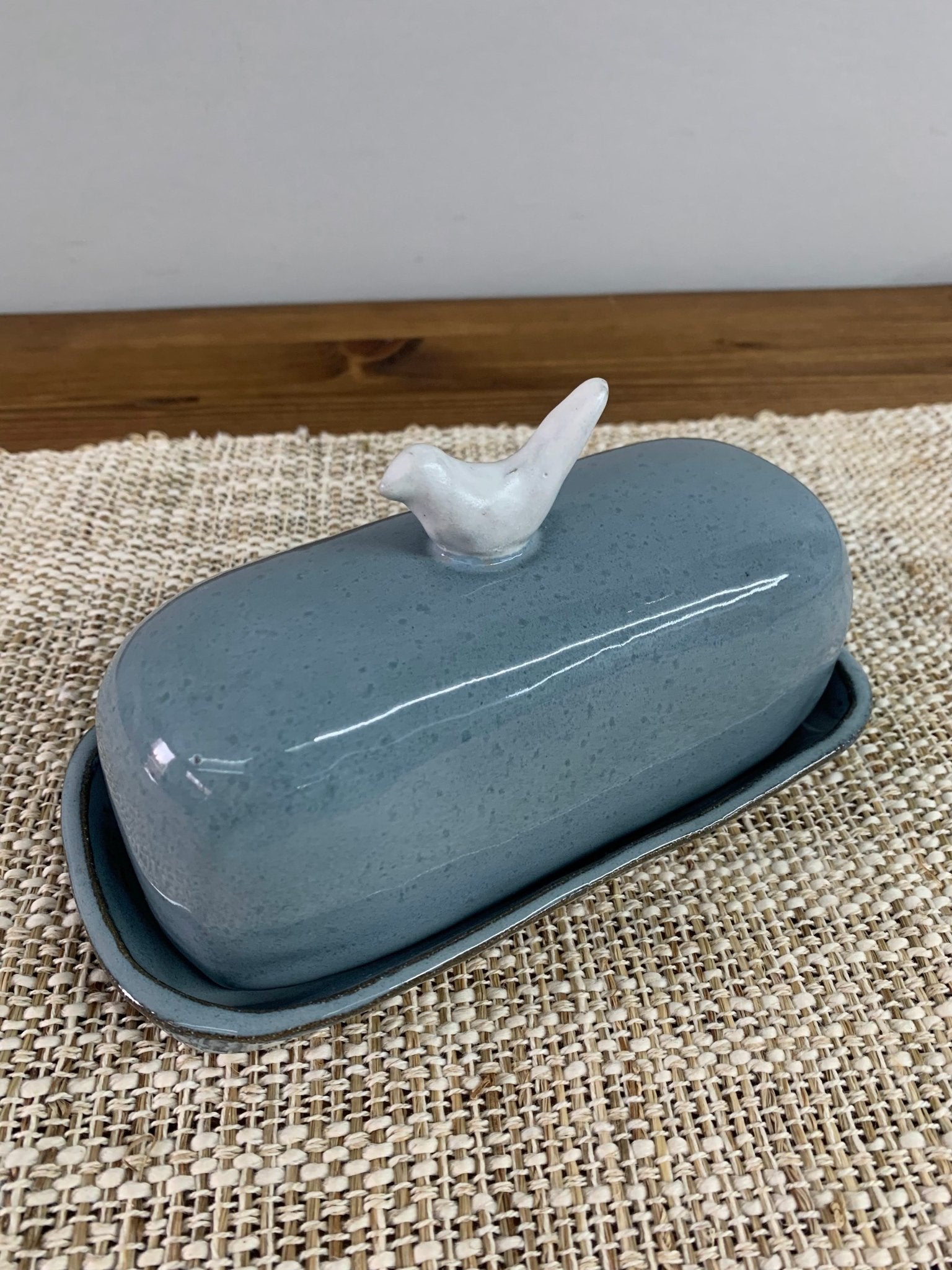 Blue ceramic butter dish with a white bird on top on a textured surface.