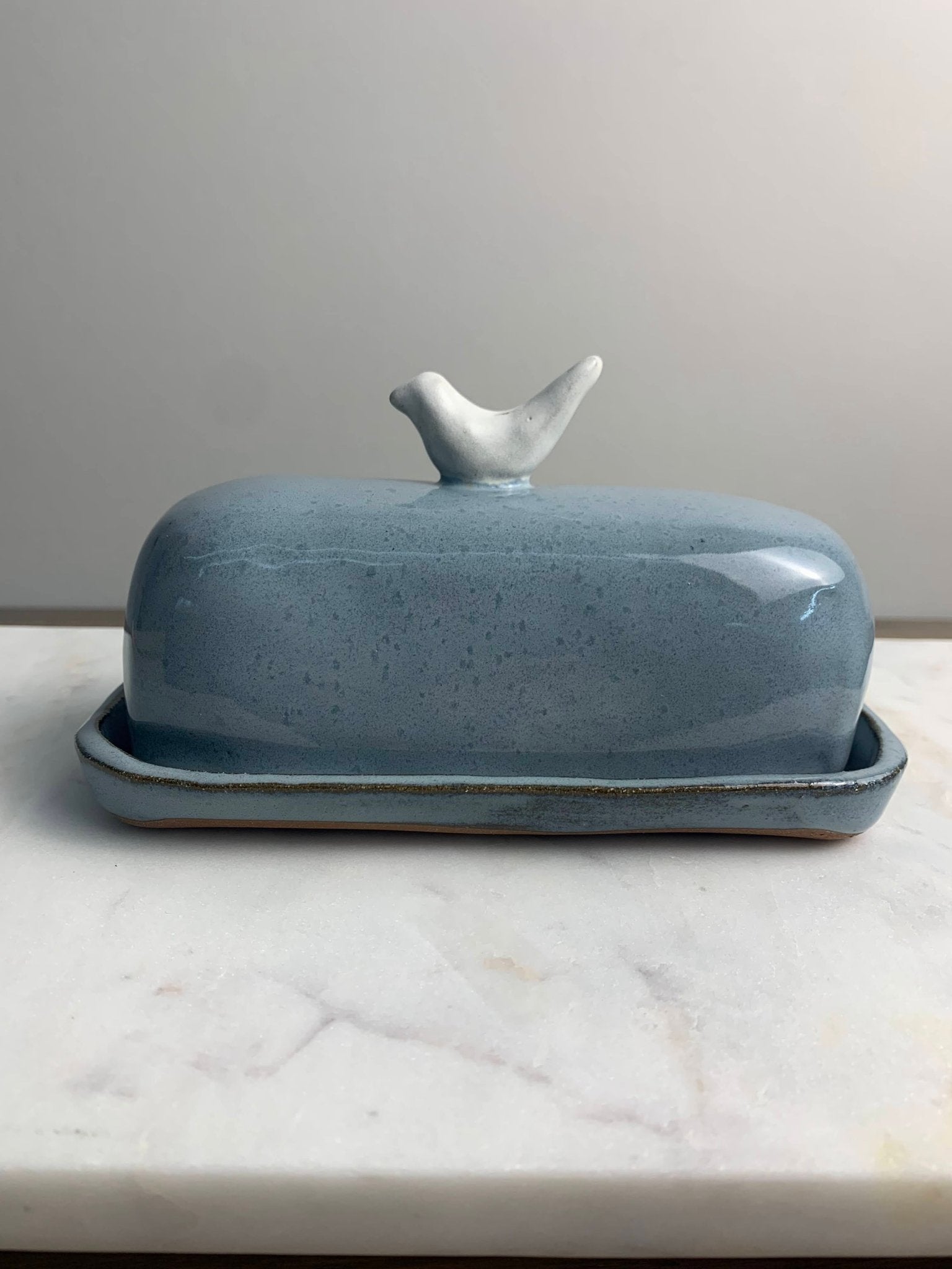 Blue stoneware ceramic butter dish with bird lid on a marble surface