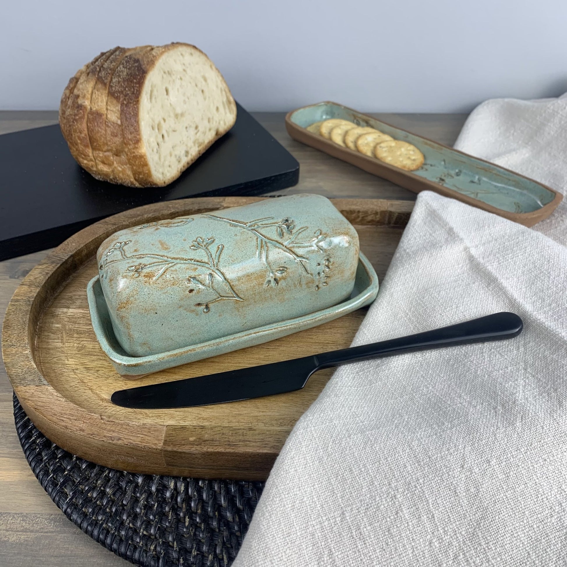 Handmade ceramic butter dish with bread and crackers on a wooden board
