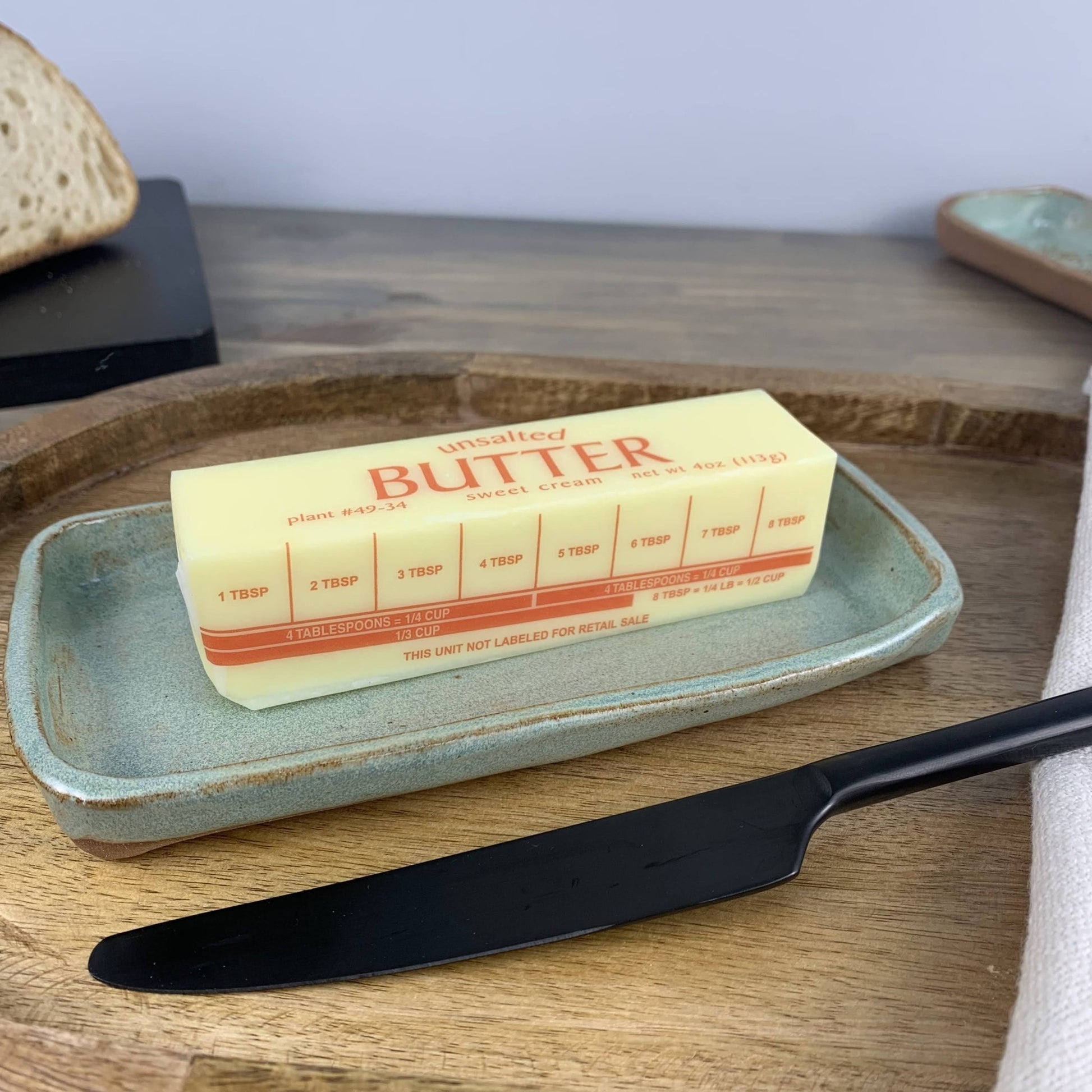 Butter stick on a ceramic tray with a knife on a wooden surface