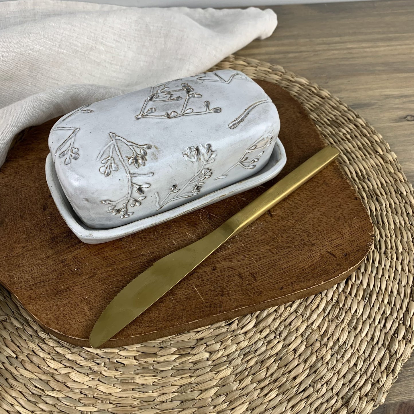 Handmade ceramic butter dish with floral patterns on a wooden board with a gold knife
