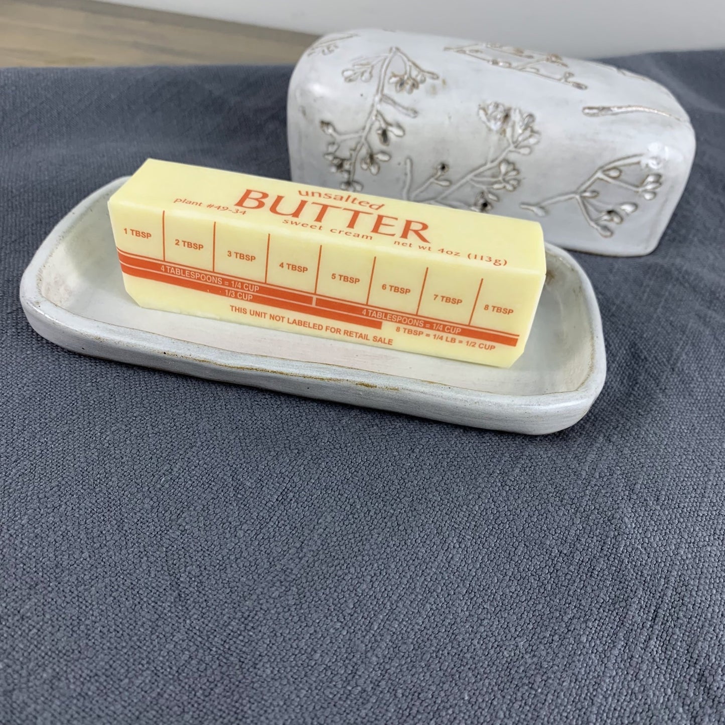 Butter stick on a white ceramic tray with a decorative lid on a gray surface
