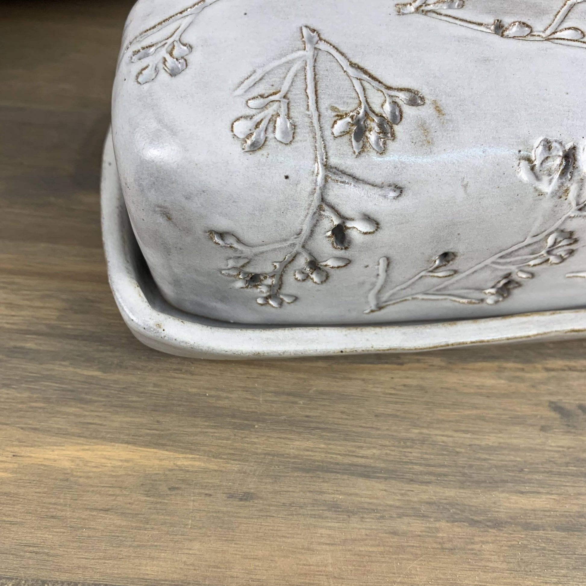 Handmade ceramic butter dish with floral patterns on a wooden surface