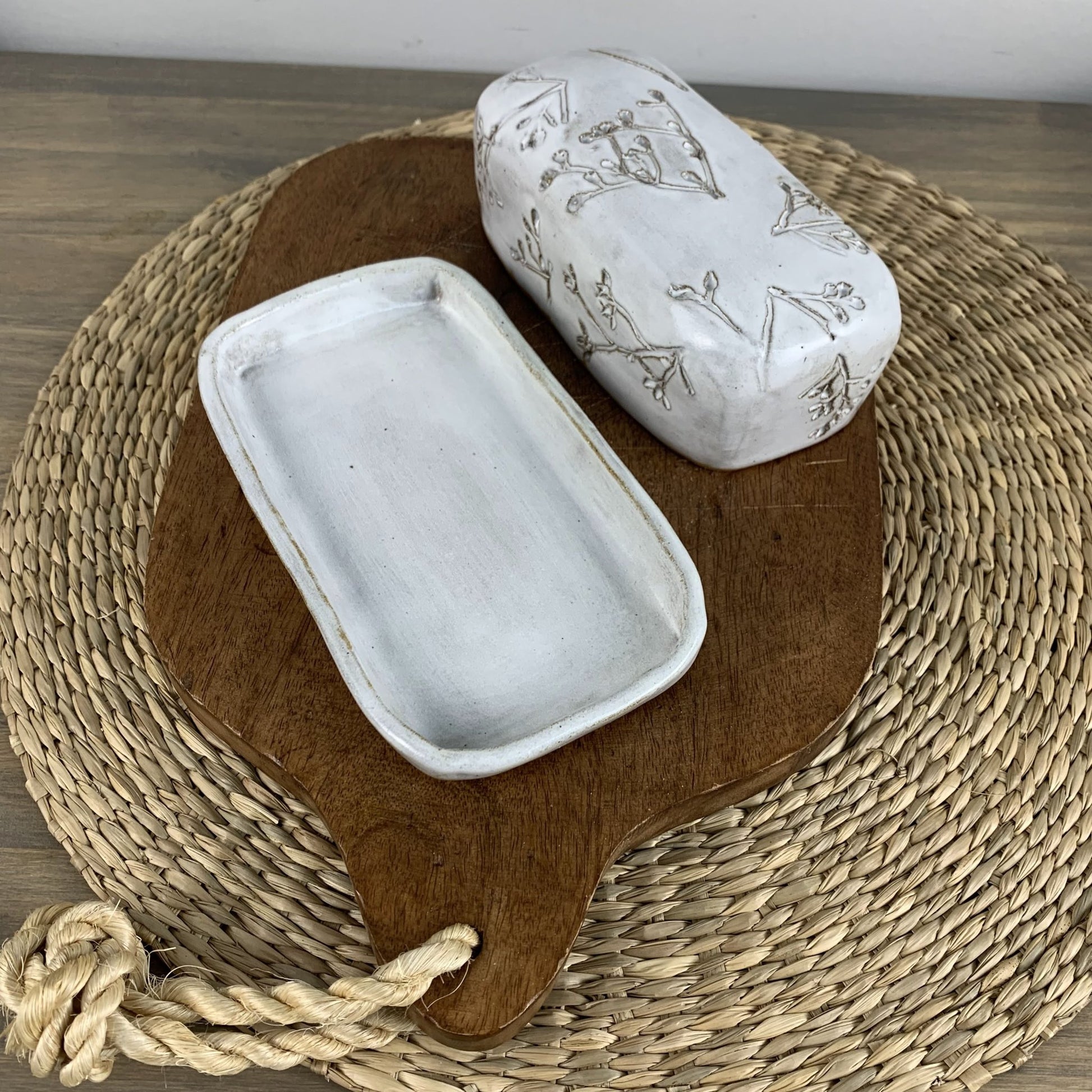 White handmade ceramic dish with floral patterns on a wooden board on a woven mat.