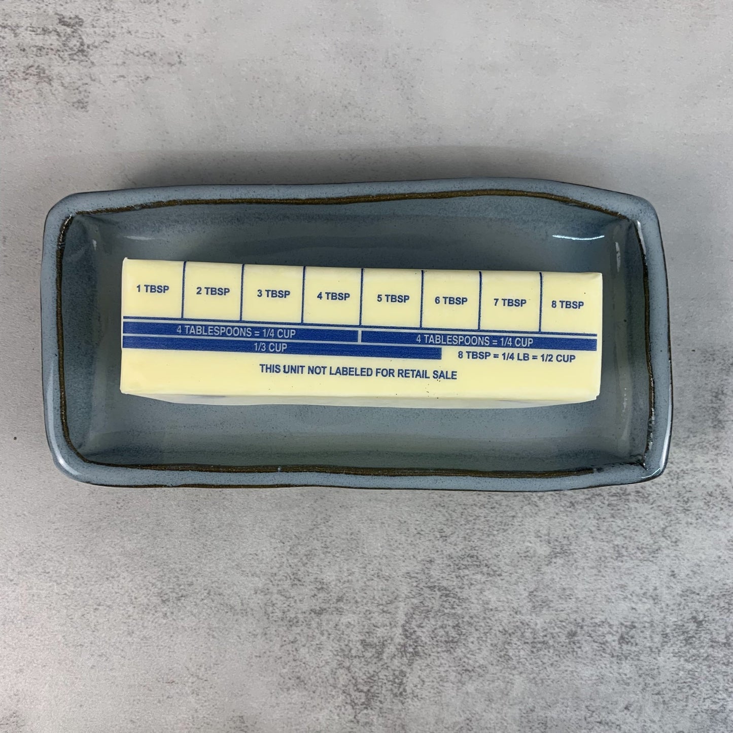 Butter stick with measurement labels in a blue ceramic butter dish on a gray surface