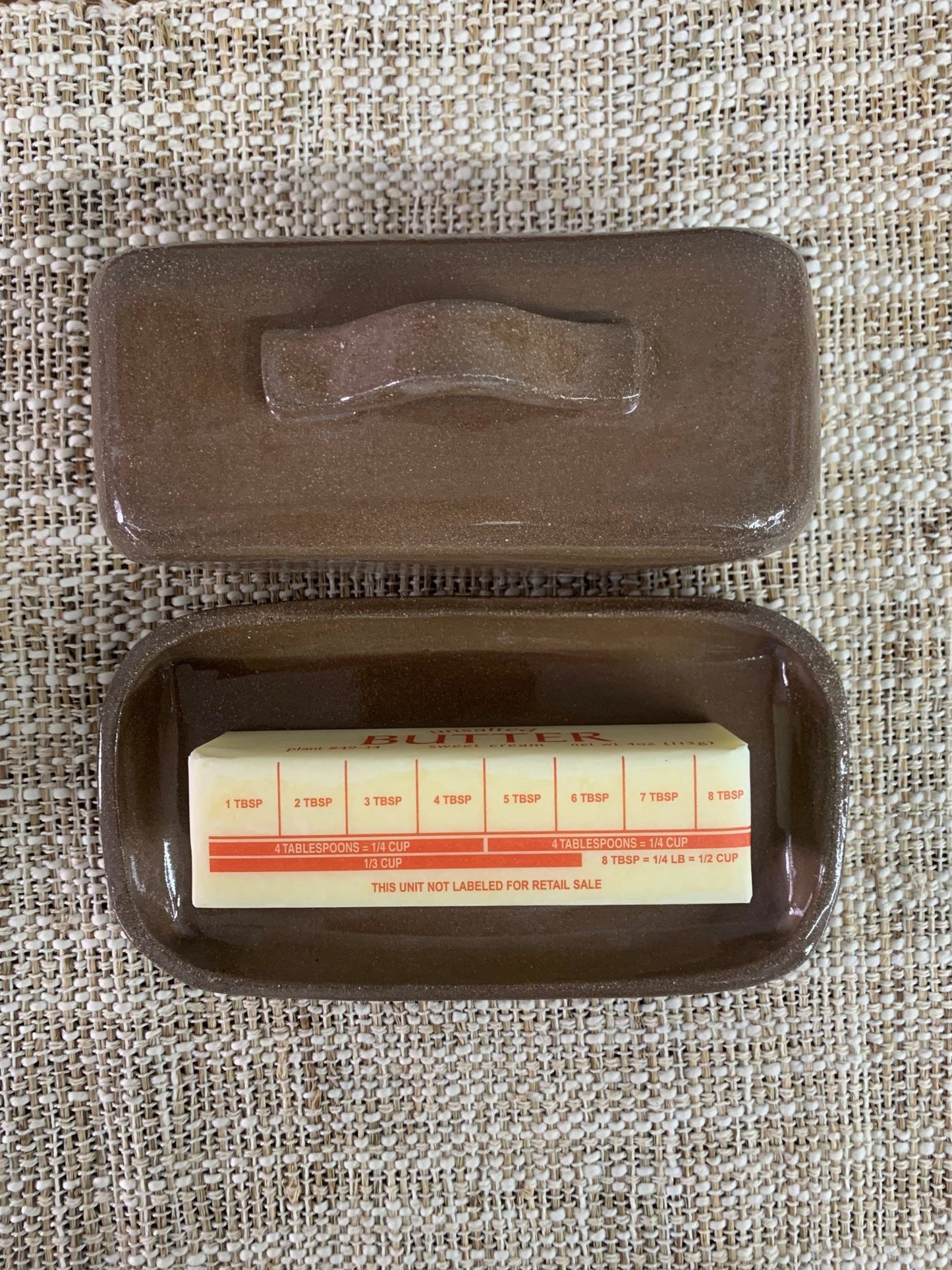 Brown handmade ceramic butter dish on textured fabric