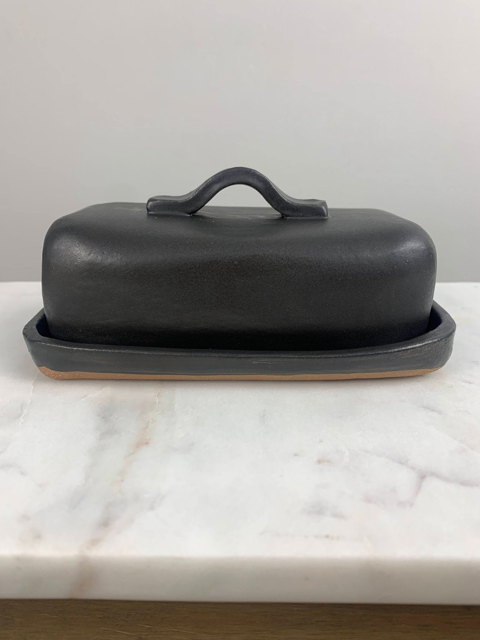 Black ceramic butter dish with lid on a marble surface