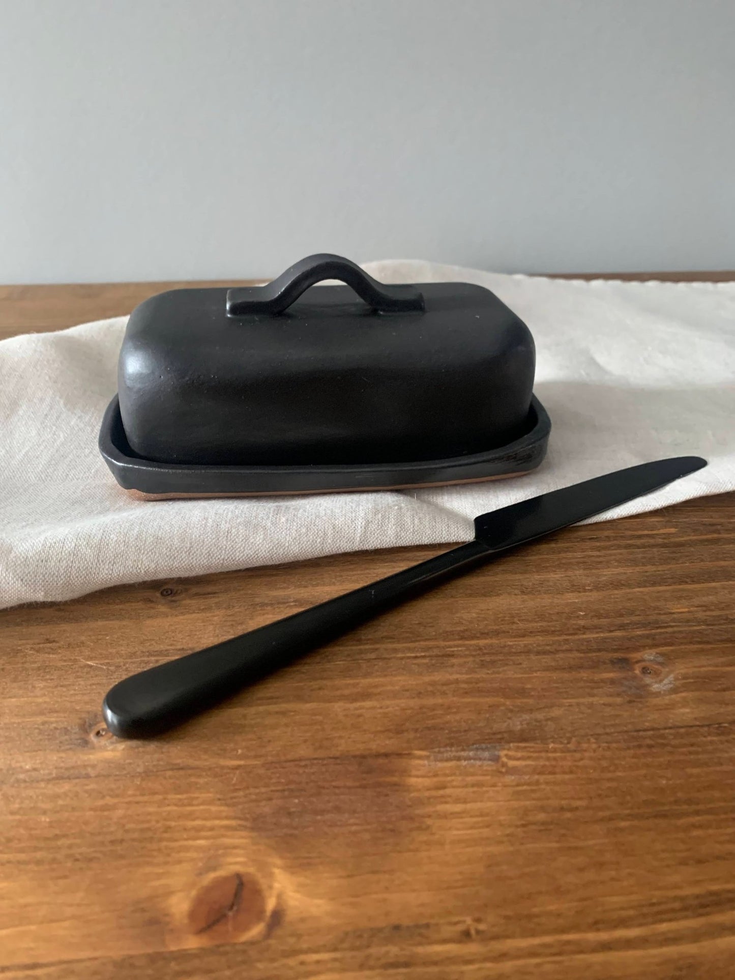 Black handmade ceramic butter dish with lid and knife on a wooden surface