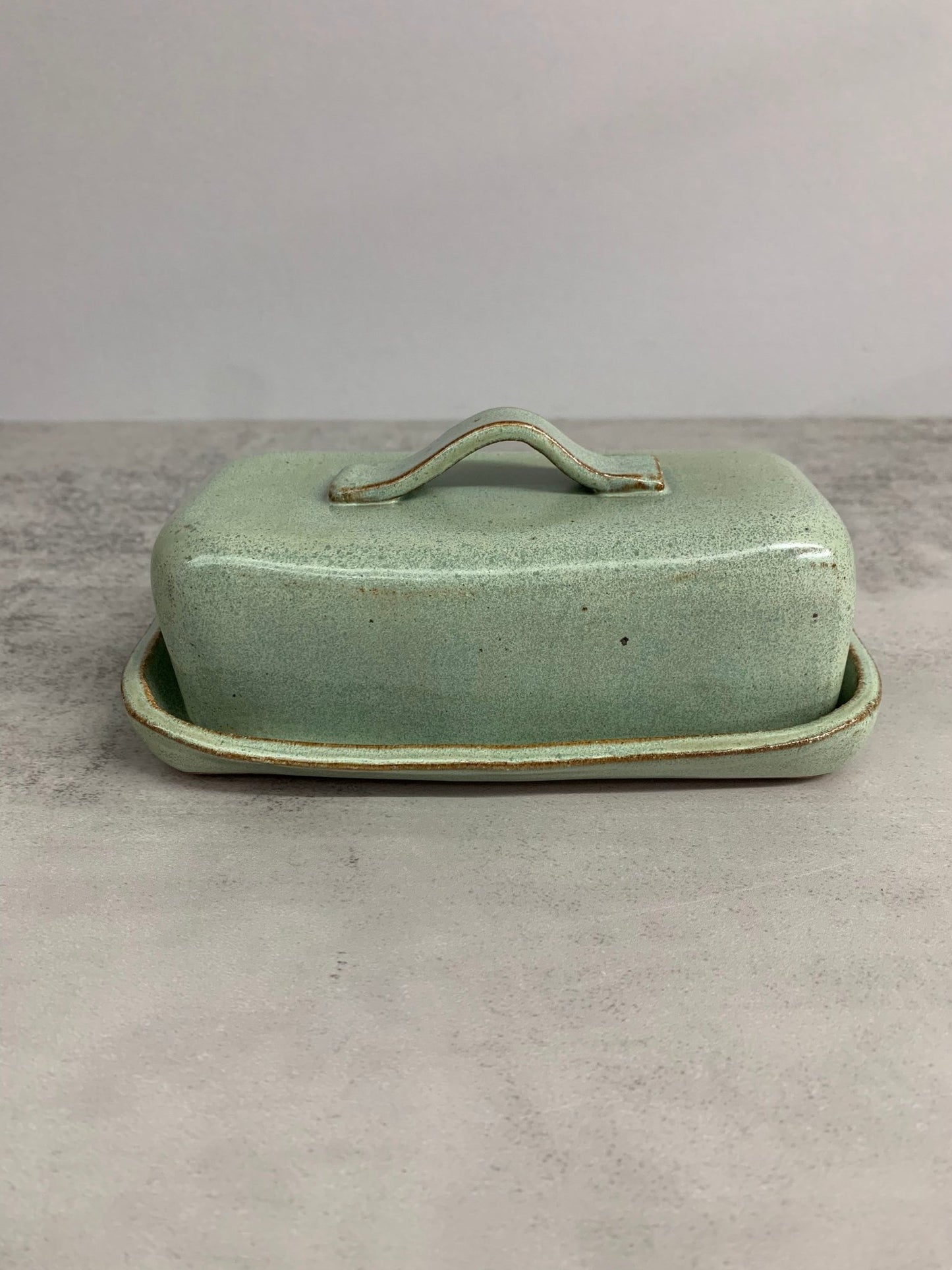 Green ceramic butter dish with lid on a gray surface