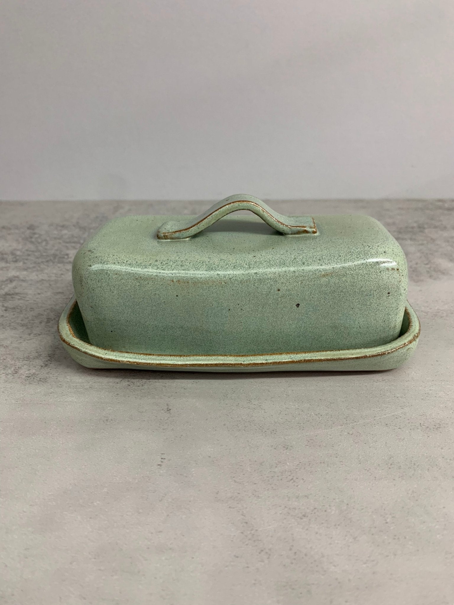 Green ceramic butter dish with lid on a gray surface