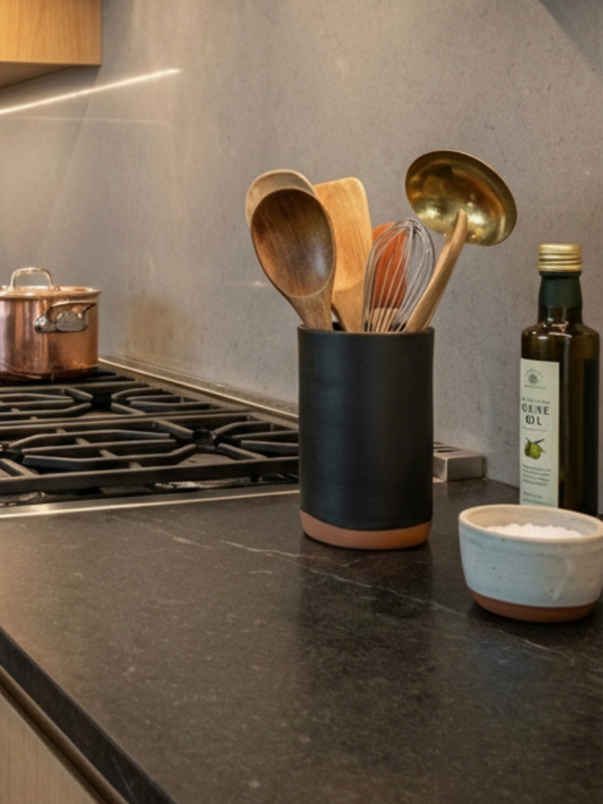 Black ceramic handmade utensil holder with wooden spoons on a kitchen counter