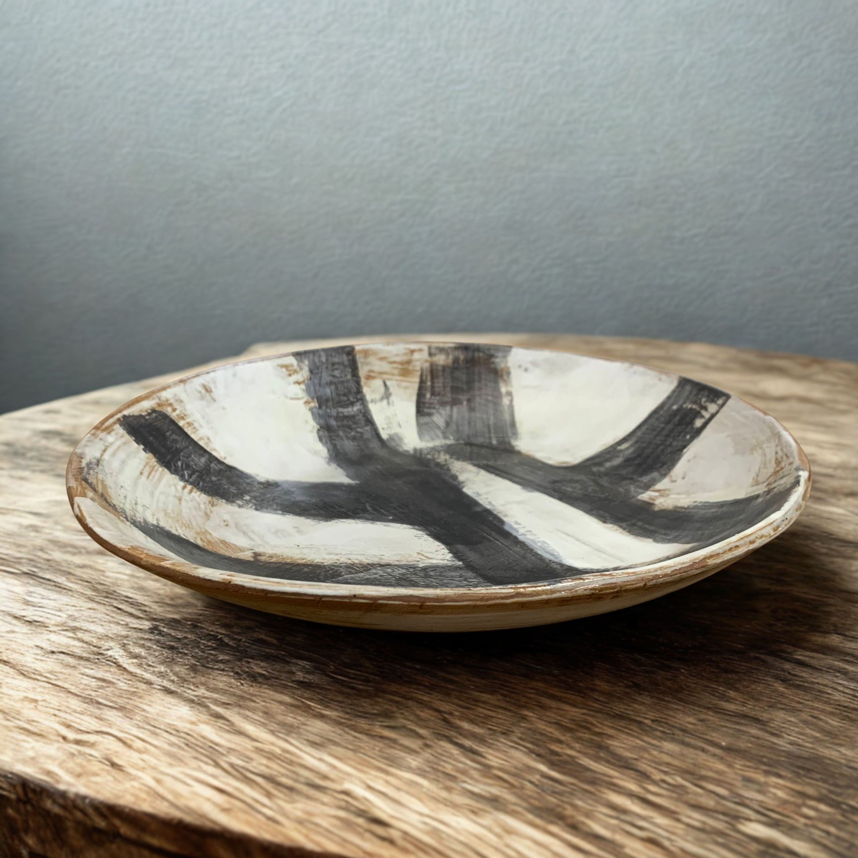 large shallow Ceramic bowl with black and white abstract painted design on a wooden surface