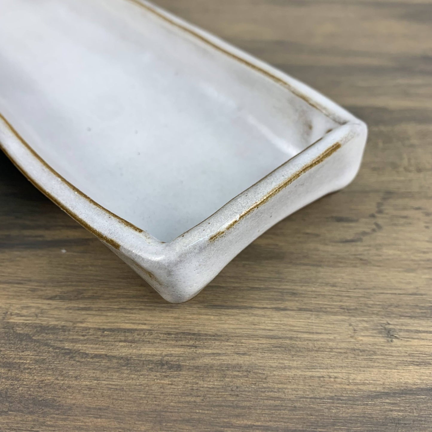 Rectangular ceramic dish with brown rim on a wooden surface