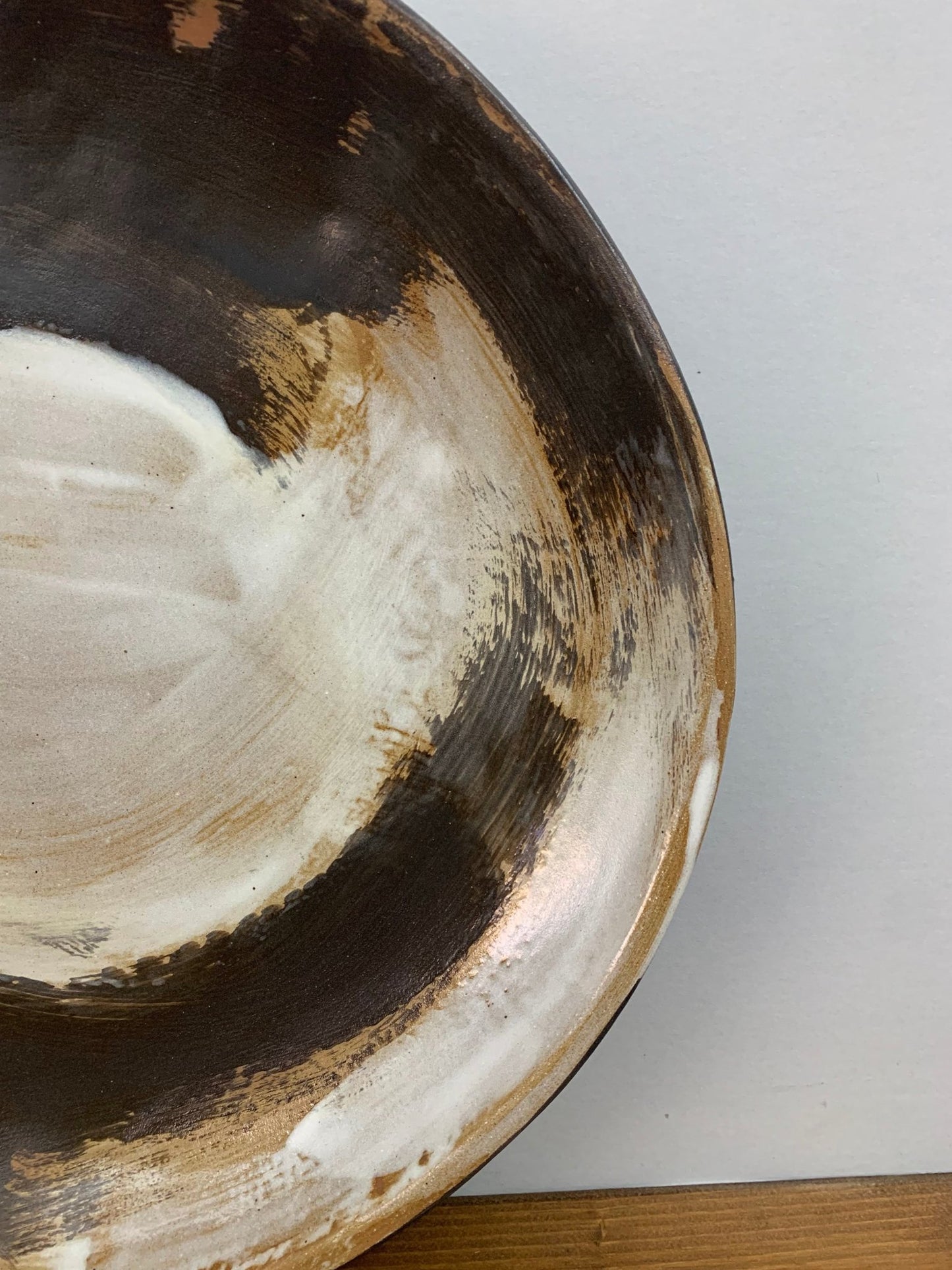 closeup of a Ceramic art bowl with expressive black and white brush strokes  on a wood surface and gray background