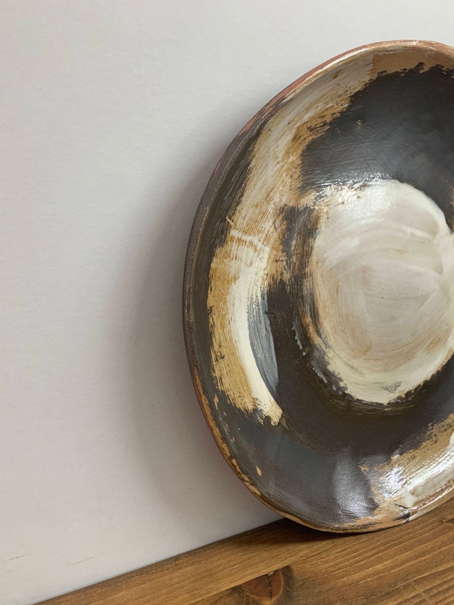 closeup angle of a Ceramic art bowl with expressive swirling black and white brush strokes  on a wood surface against gray wall