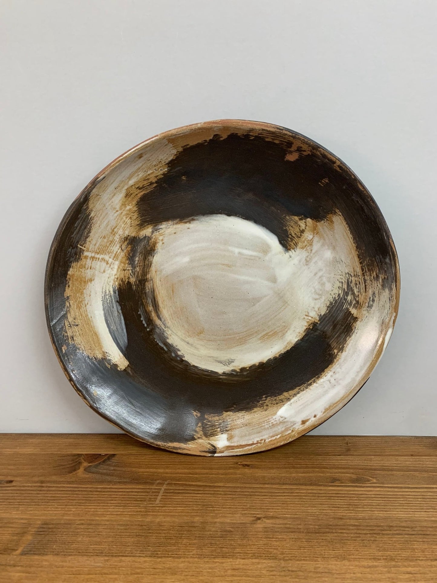 handcrafted Ceramic art bowl with expressive swirling black and white brush strokes  on a wood surface against a gray wall