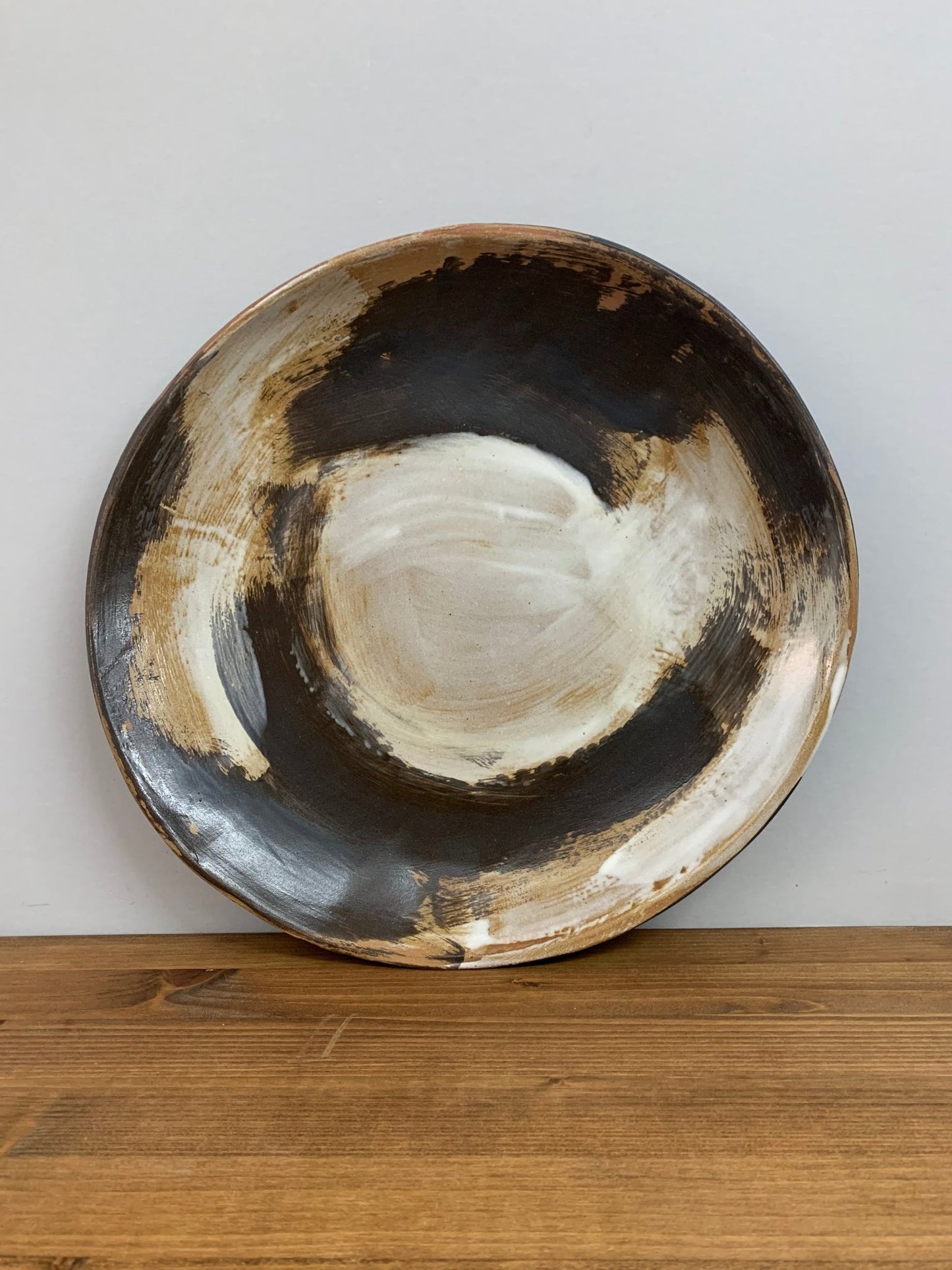 Ceramic art bowl with expressive swirling black and white brush strokes  on a wood surface leaning against gray wall