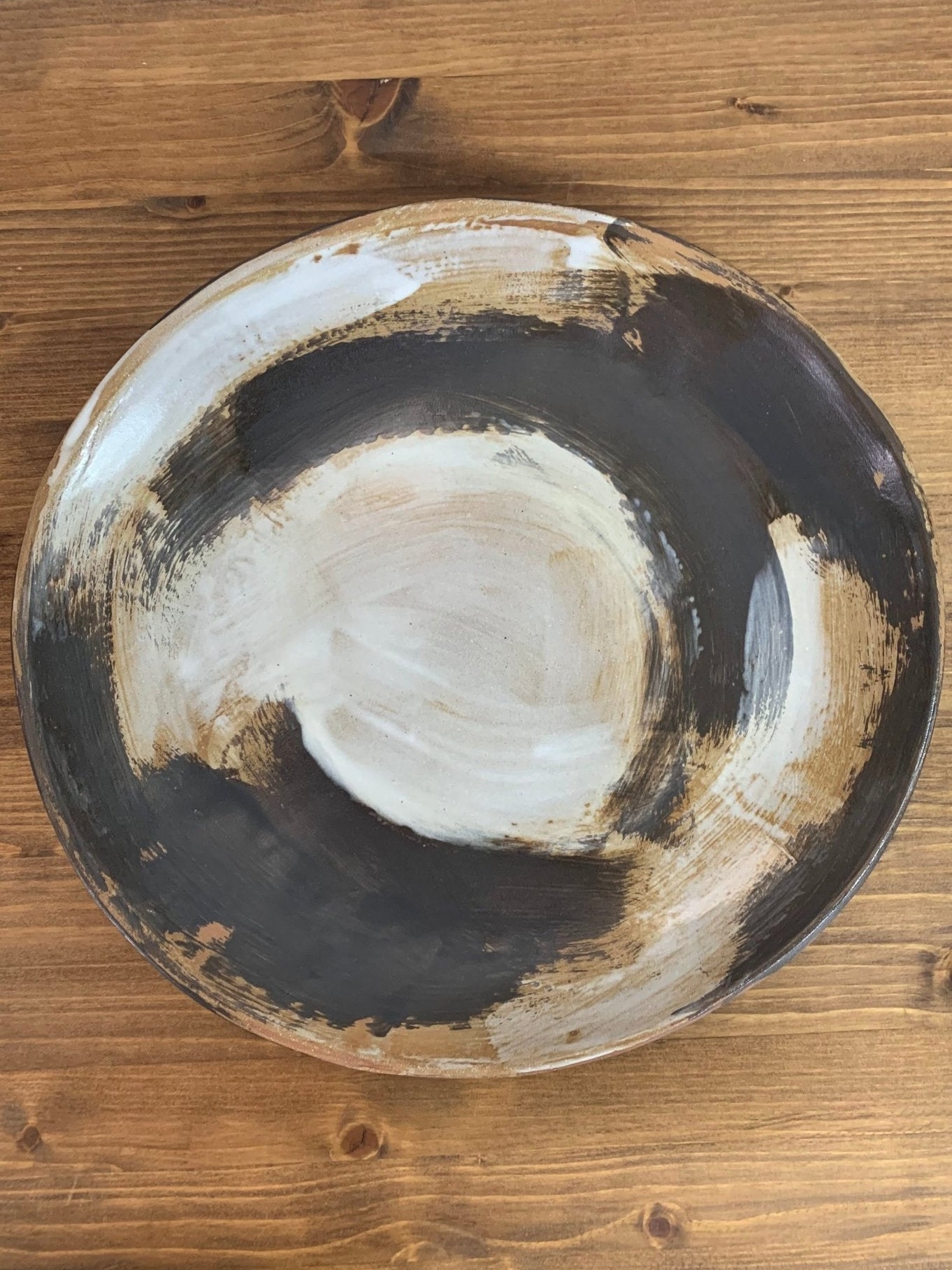 Ceramic art bowl with expressive swirling black and white brush strokes  on a wood surface