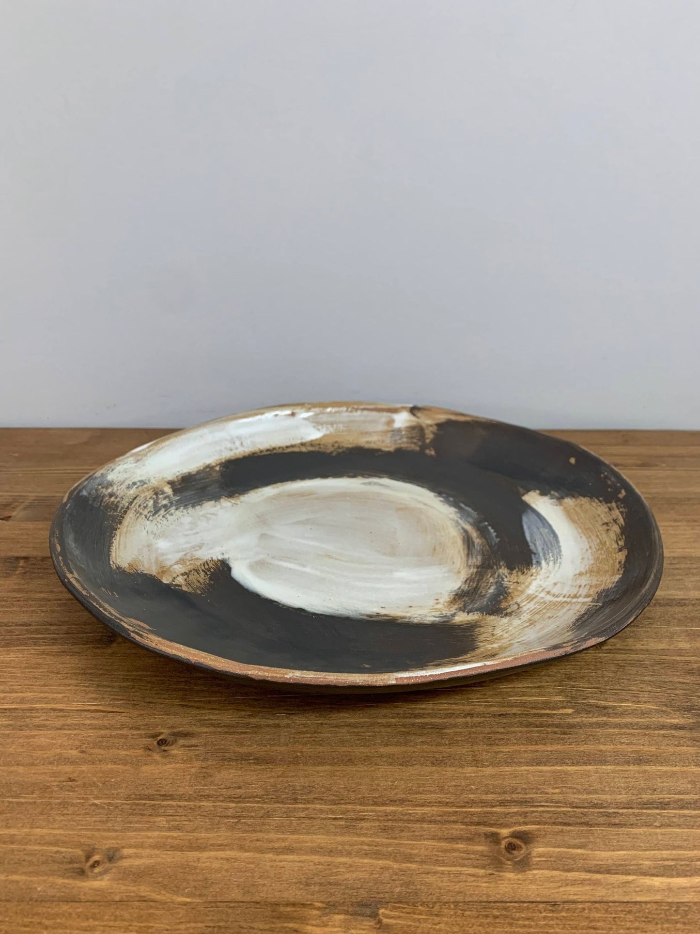 Ceramic art bowl with expressive swirling black and white brush strokes  on a wood surface with gray background