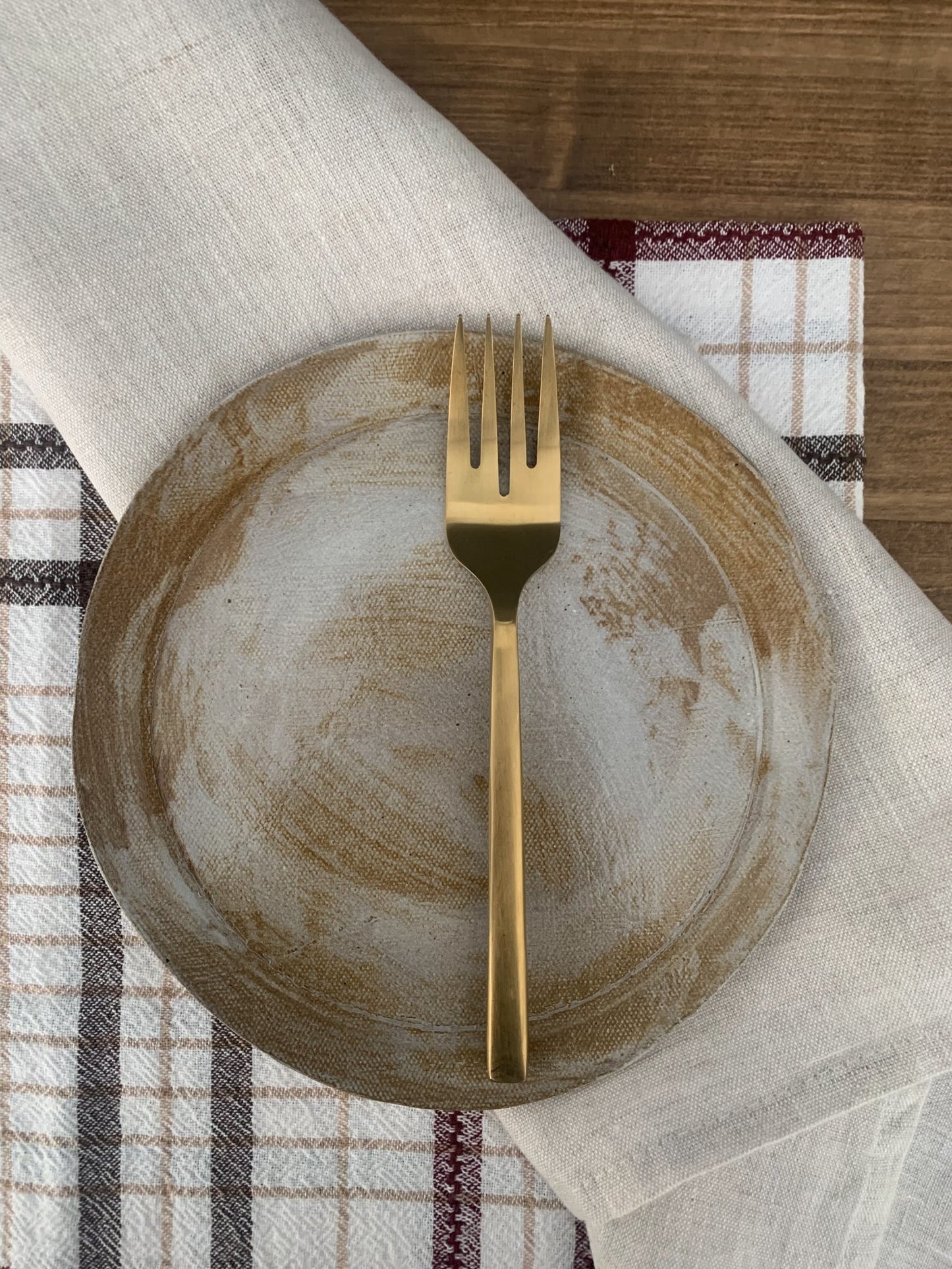Gold fork on a handmade ceramic plate with a checkered tablecloth