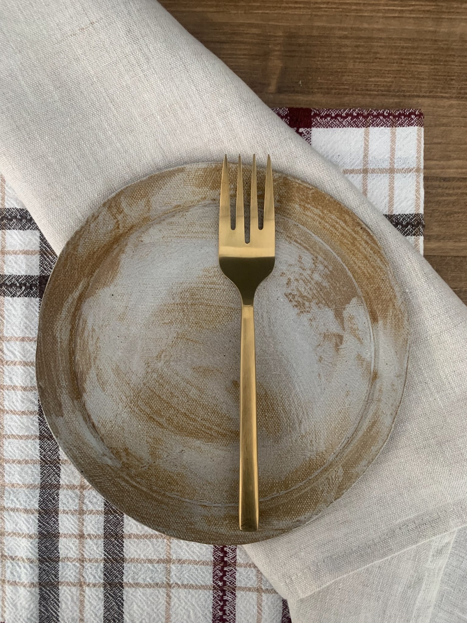 Gold fork on a handmade ceramic plate with a checkered tablecloth