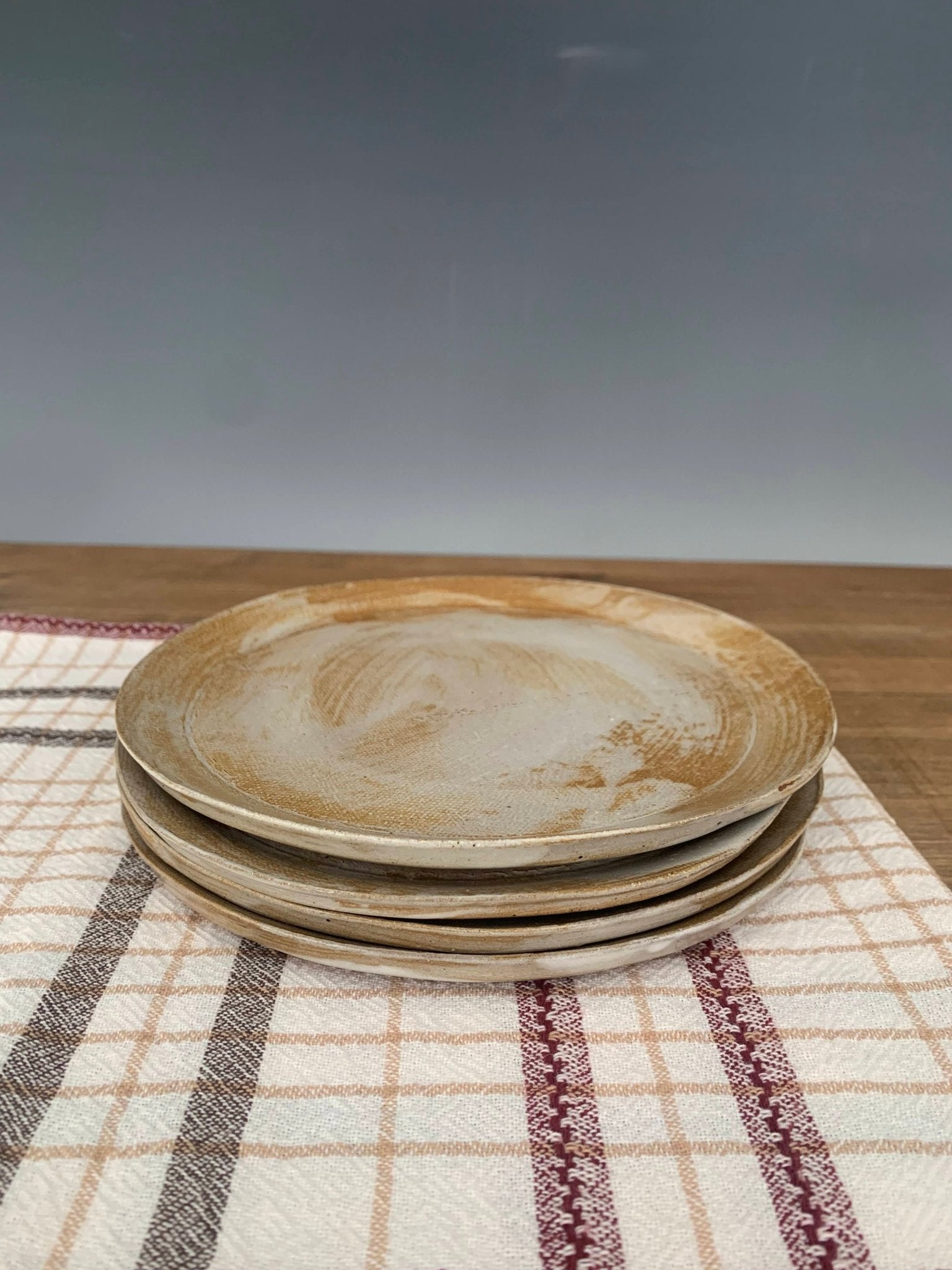 Stack of handmade stoneware dishes on a checkered tablecloth with a blurred background