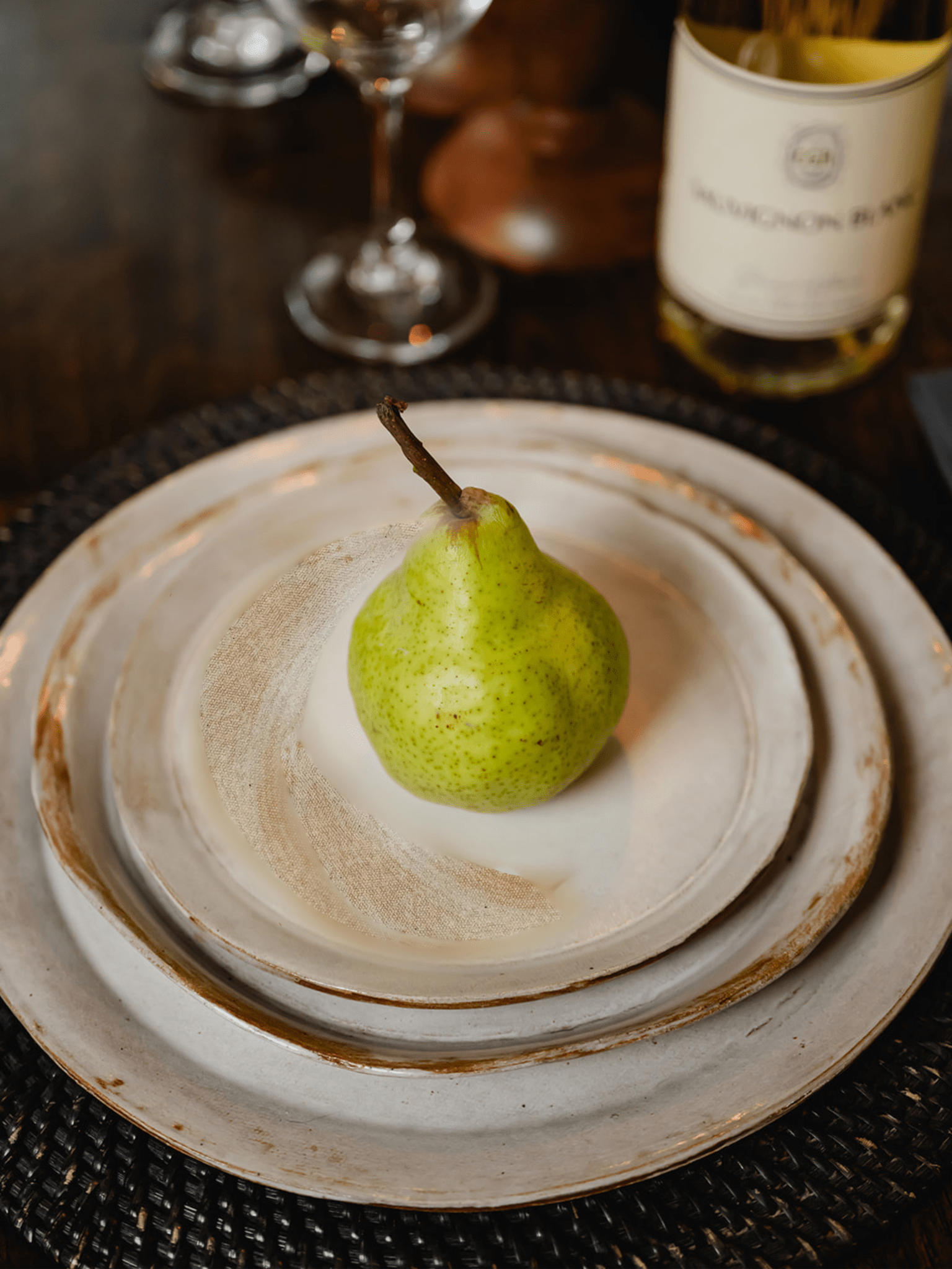 Stack of three irregular plates on a dinner table with a pear on top