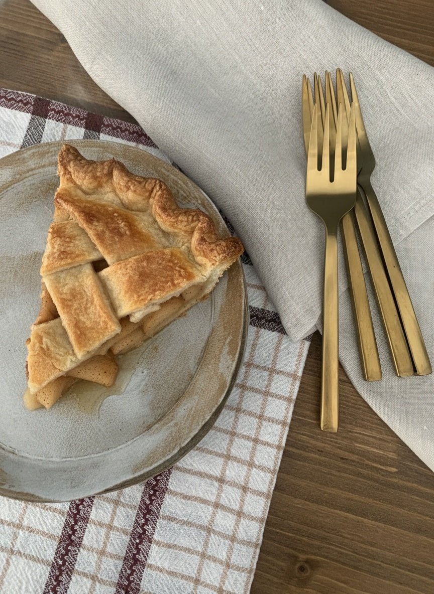 Slice of pie on a handmade ceramic plate with gold forks on a wooden table