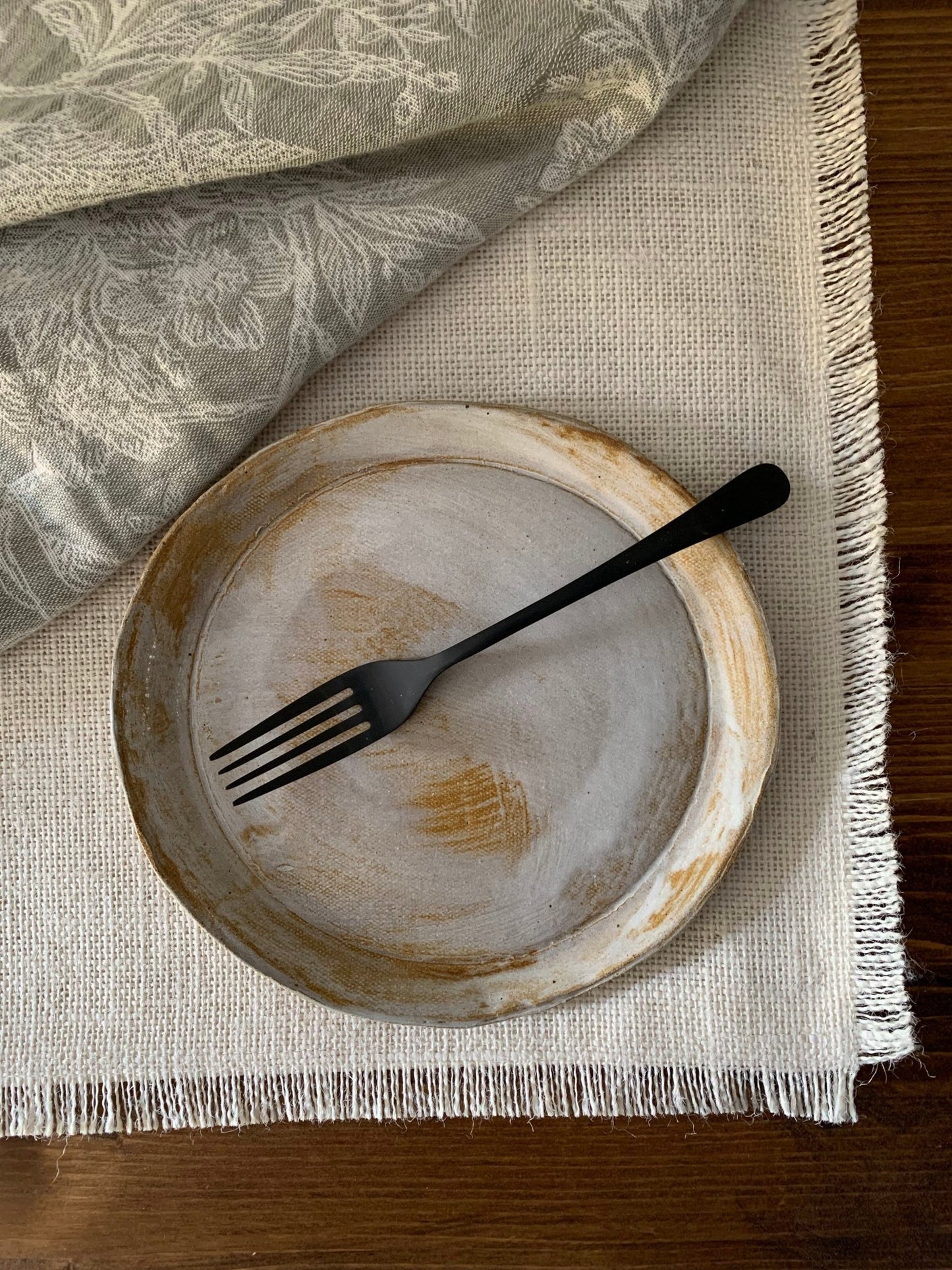 Handmade ceramic plate with a black fork on a textured fabric surface