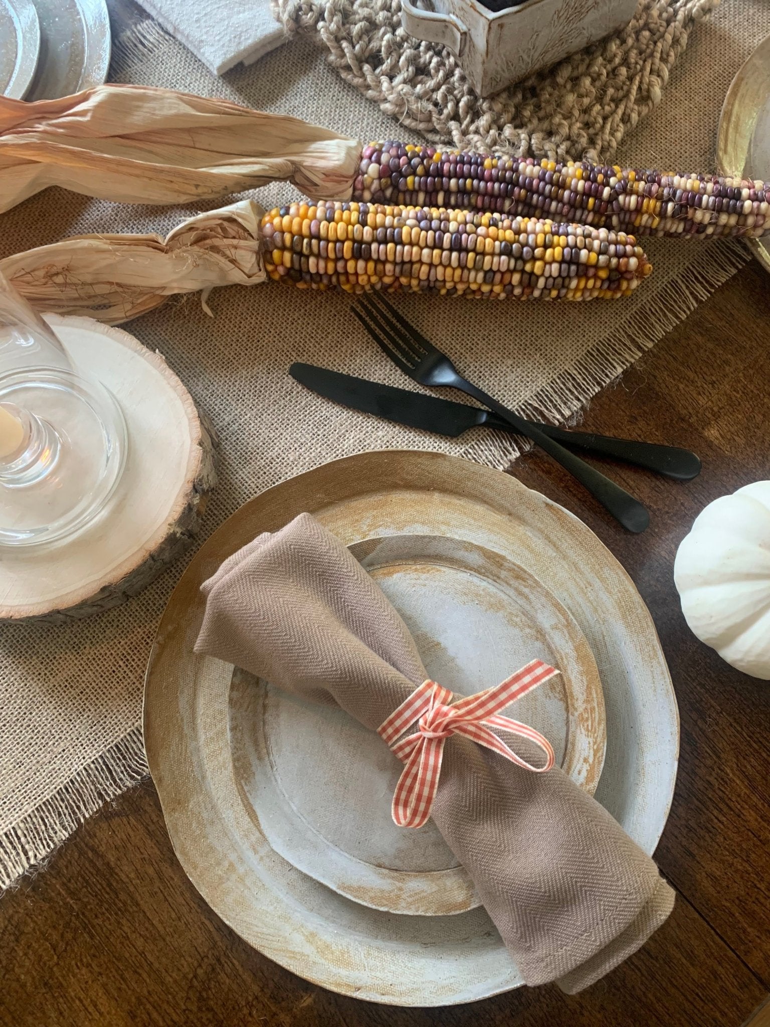 Table setting with handmade ceramic dinnerware, napkin, and corn on a wooden table.