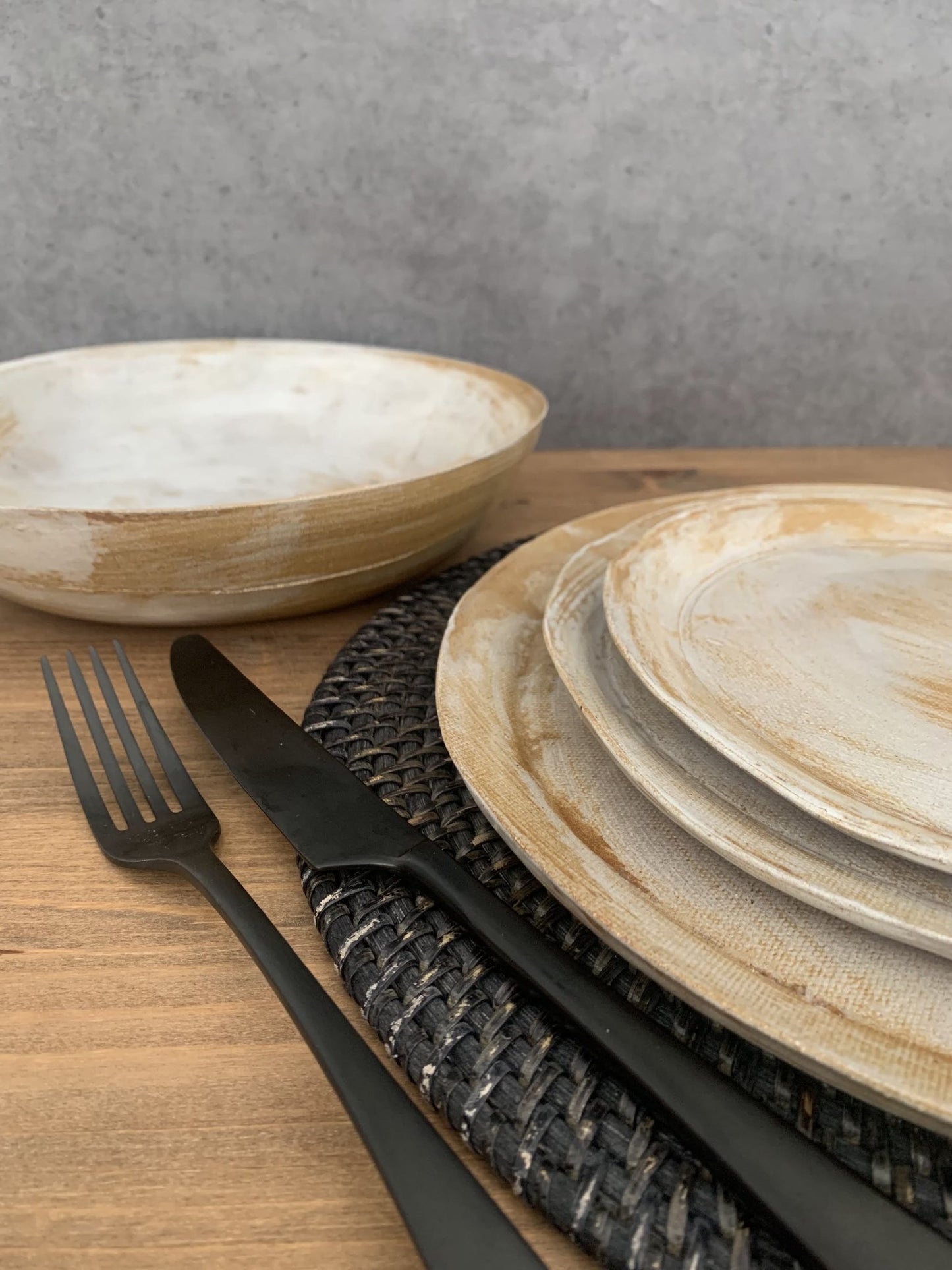 Set of handmade ceramic plates and bowls with black cutlery on a wooden surface.
