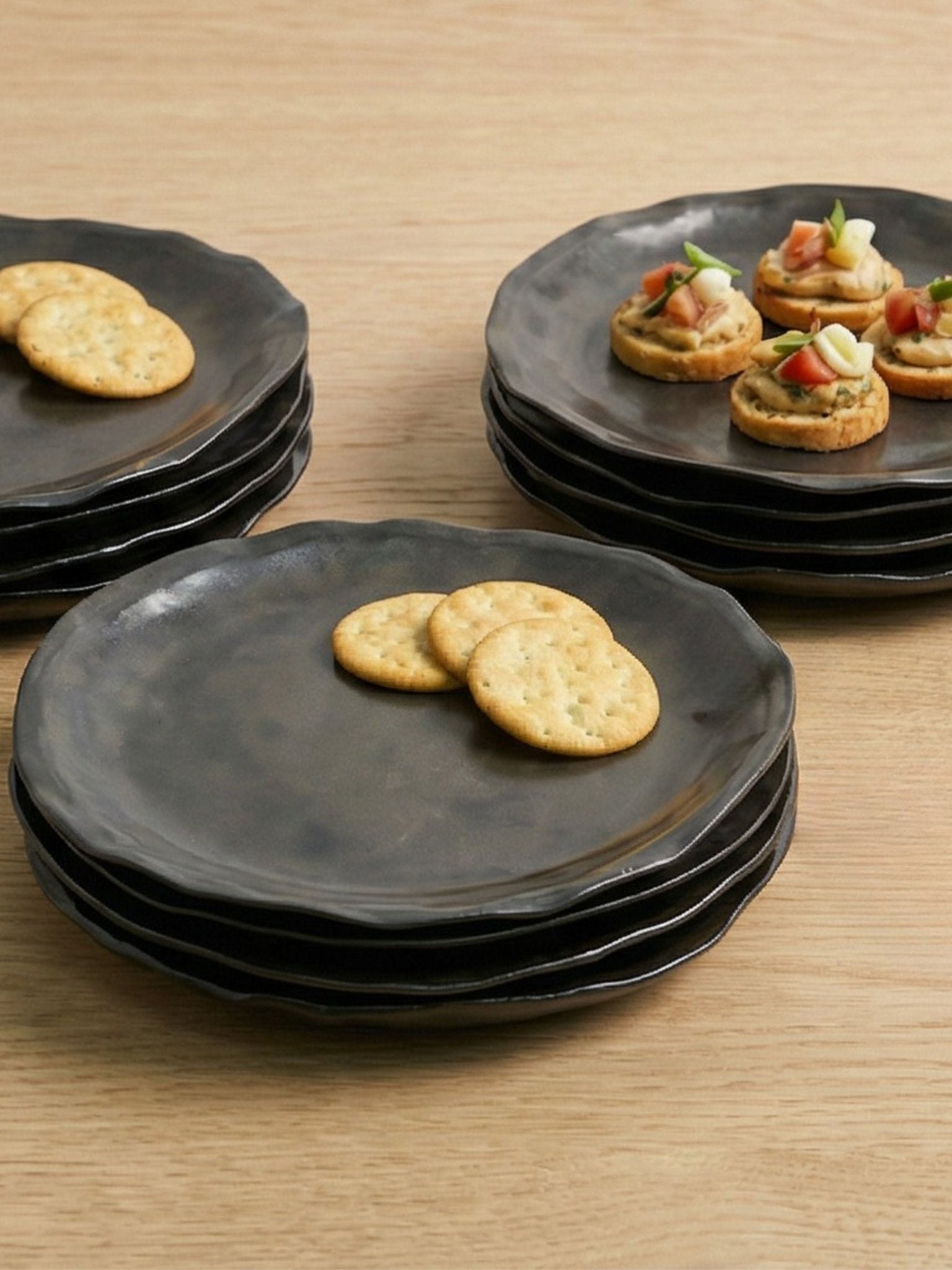 Stacks of brown handcrafted plates with crackers and small appetizers on a wooden surface